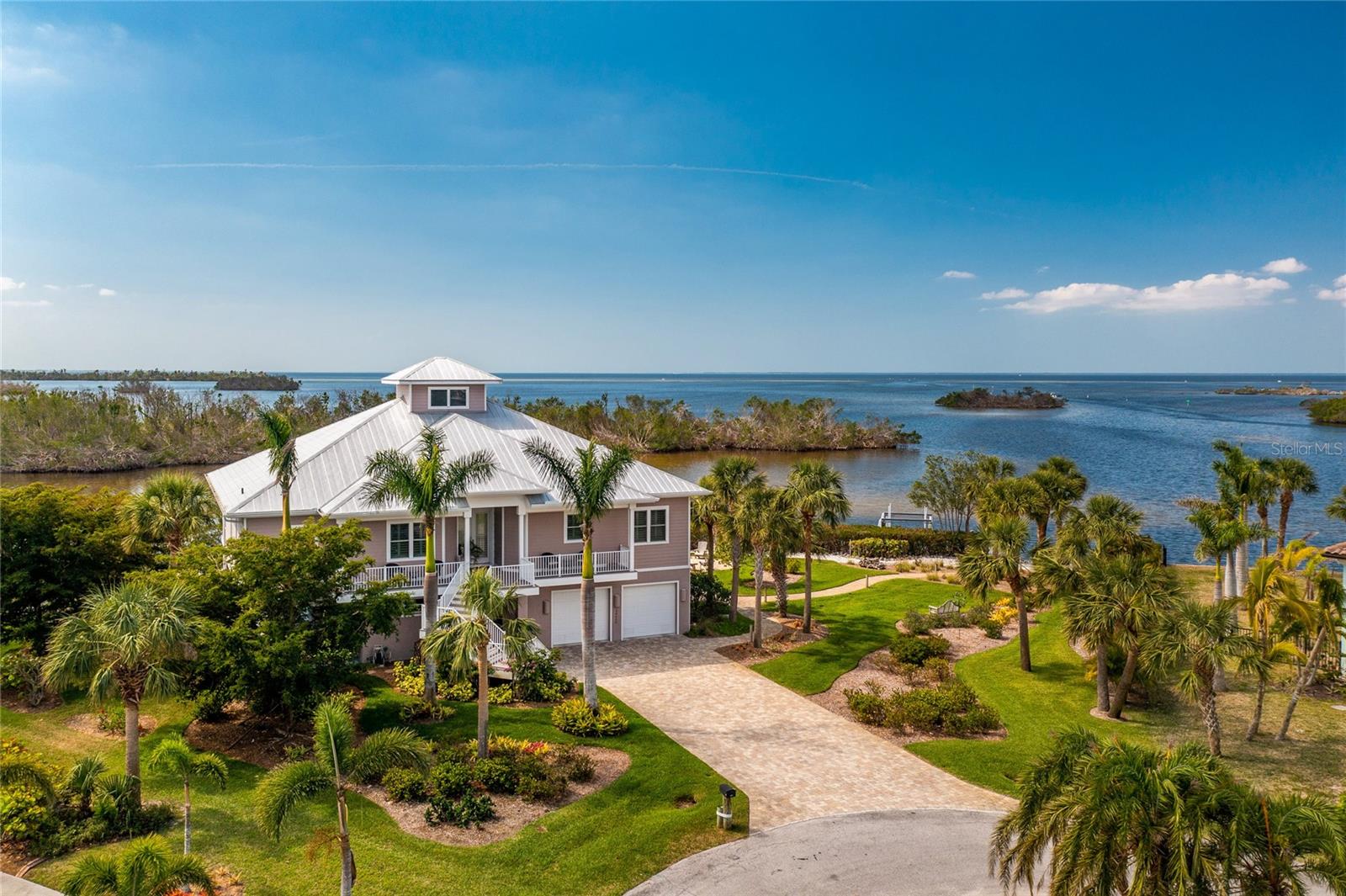 A modern twist on old Florida living - this waterfront oasis is truly the treasure of Pirate Harbor! Overlooking the untouched estuary of Charlotte Harbor with pristine grounds and inviting outdoor living spaces, it will feel like the colorful nightly sunsets are a private show - just for you!
Boasting over 275 feet of water frontage, a private tiki hut, dock, lift, and kayak launch, you can live each day as an adventure when you live on Treasure Island! If you arrive by car, you will be greeted by a long paver driveway surrounded by lush tropical vegetation leading you up the stairs to your Key West-style dream home. Inside, you will be welcomed by an expansive open floorplan with 10-12 foot ceilings, and a dramatic wall of windows connecting you with Charlotte Harbor beyond. Modern and timeless, this chef's kitchen is a showstopper! The dual-tone Euro-style flat panel cabinetry is topped with Oakhampton Cambria Quartzite counters, creating the ideal venue for whipping up a culinary masterpiece. Guests will gather at the generous breakfast bar as you make use of the 36" Wolf gas cooktop and prep sink in the adjoining island - complete with ample drawers to house all of your cookware. The in-wall oven and convection/ microwave are surrounded by a wall of cabinetry. An expansive walk-in butler's pantry provides abundant storage. Staggered walnut tile leads you into the formal dining space and living room, where the solid wood built-in entertainment center, complete with sliding door, discreetly hides away your television. A built-in window seat is nestled between dual French doors leading to two open-air decks- the perfect venue to sip your morning coffee while the birds play on the sandbar. The owner's suite enjoys endless water views through the windows and 8' sliding glass doors which lead to the outdoor living space. Spacious custom closets and luxurious ensuite bath make this a true sanctuary - complete with soaking tub, frameless walk-in shower with pebble mosaic floor, and floating vanities with Euro-style flat panel cabinetry and underlighting. Visitors may never want to leave their private guest wing, consisting of two cheerful bedrooms, sliders to the deck with water views, and bathroom with frameless tiled shower. After a day on the water, head down the iron and walnut staircase and spend the evening relaxing in the breathtaking outdoor living space. Take a dip in the glistening pool, relax in the heated spa, or sip a drink on the expansive paver pool deck. The waterfront fire pit is the ideal spot for friends and family to gather together, share stories and make memories. There is no shortage of storage space in this home, with the lower level being devoted to a three car tandem garage, multiple storage spaces, and a hobby room with mini split A/C. Laundry is no chore in the spacious utility and laundry room, with extra refrigerator, dumbwaiter to the garage, and lots of storage and counter space! Come and go with peace of mind - with full home impact doors and windows. This spectacular property is not just a home - it’s a whole new way of living!