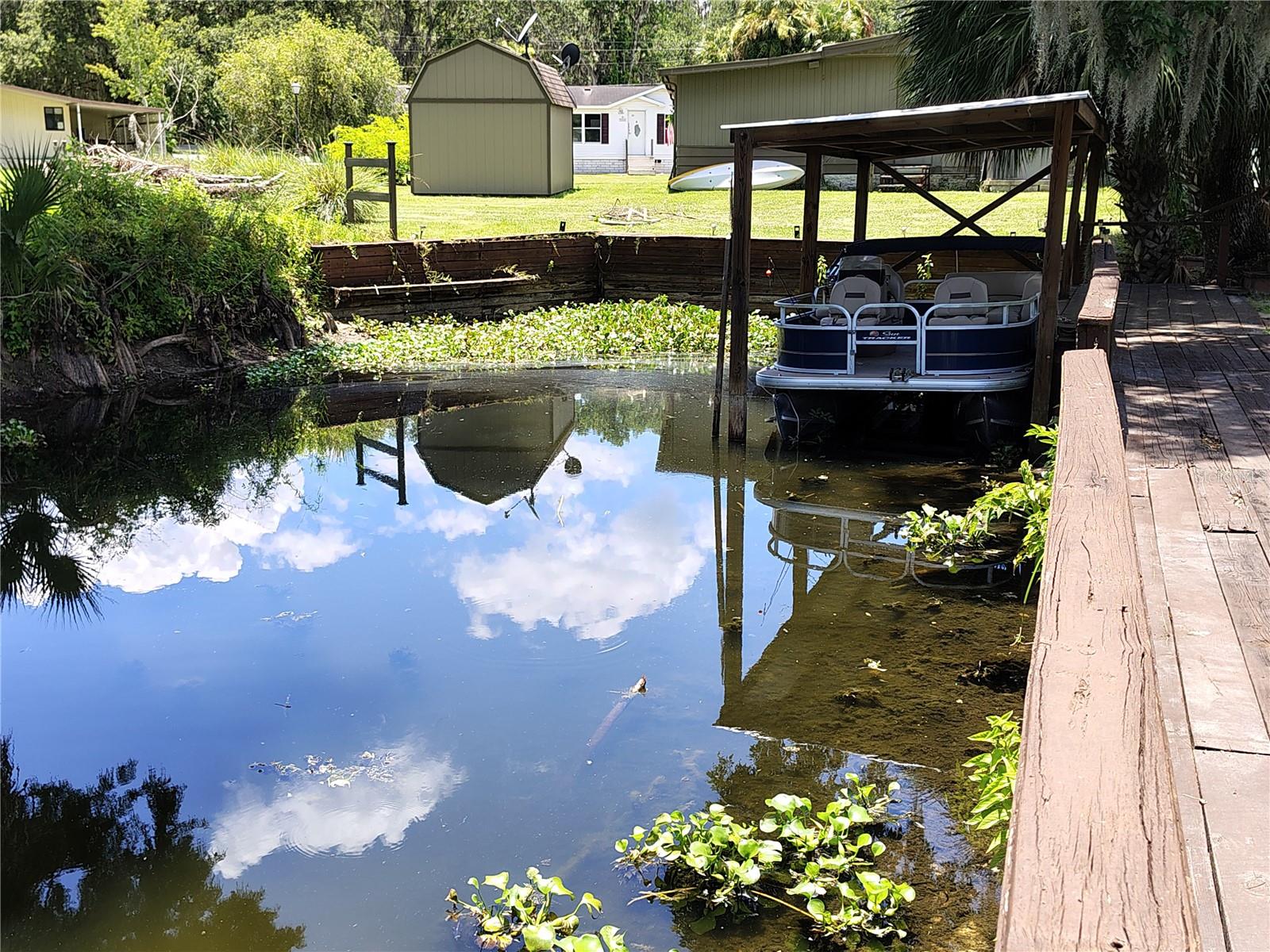 Nestled along a peaceful canal that leads directly to the beautiful Lake Panasoffkee and the Withlacoochee River, this charming 2-bedroom, 2-bath home is perfect for those who love the outdoors. Step inside and enjoy the comfort of spacious living areas, a cozy Florida room ideal for relaxing year-round, and a workshop perfect for hobbies or extra storage. With a little TLC and some updates needed. This home features a spacious, functional kitchen complete with a generously sized island and a designated dining area- perfect for everyday meals or entertaining guests. The home has a separate laundry room that leads out to an oversized covered carport. It comes mostly furnished, making for an easy move-in. Additional highlights include a durable metal roof and a newer central air and heat system for year-round comfort. The property is equipped with its own sprinkler system – perfect for maintaining flower beds or garden oasis.
Step outside with your morning coffee and unwind in the tranquil gazebo overlooking the water. From here, enjoy sitting by the water or stroll down to your private dock that provides access to Lake Panasoffkee and the beautiful Withlacoochee River.
Lake Panasoffkee is known for some of the best fishing in Florida—whether you're casting for bass or panfish, you'll find plenty to keep you hooked. The Withlacoochee River is a haven for canoeing, boating, air boating, and spotting abundant birds and wildlife. It's a nature lover’s dream come true.
Whether you're seeking a weekend retreat or a full-time residence, this home provides the perfect blend of comfort, adventure, and natural beauty. For all outdoor enthusiasts, this is your chance to live in the Florida lifestyle—right at your doorstep. Just minutes away, The Villages hosts free nightly entertainment, golf, shopping, dining, and much more! Florida’s west coast is nearby with waterfront dining, kayaking, fishing, beaches, and springs for weekend fun. Easy access to I-75 and the Florida Turnpike makes trips to Orlando’s theme parks and airports a breeze. Equal Housing Opportunity.