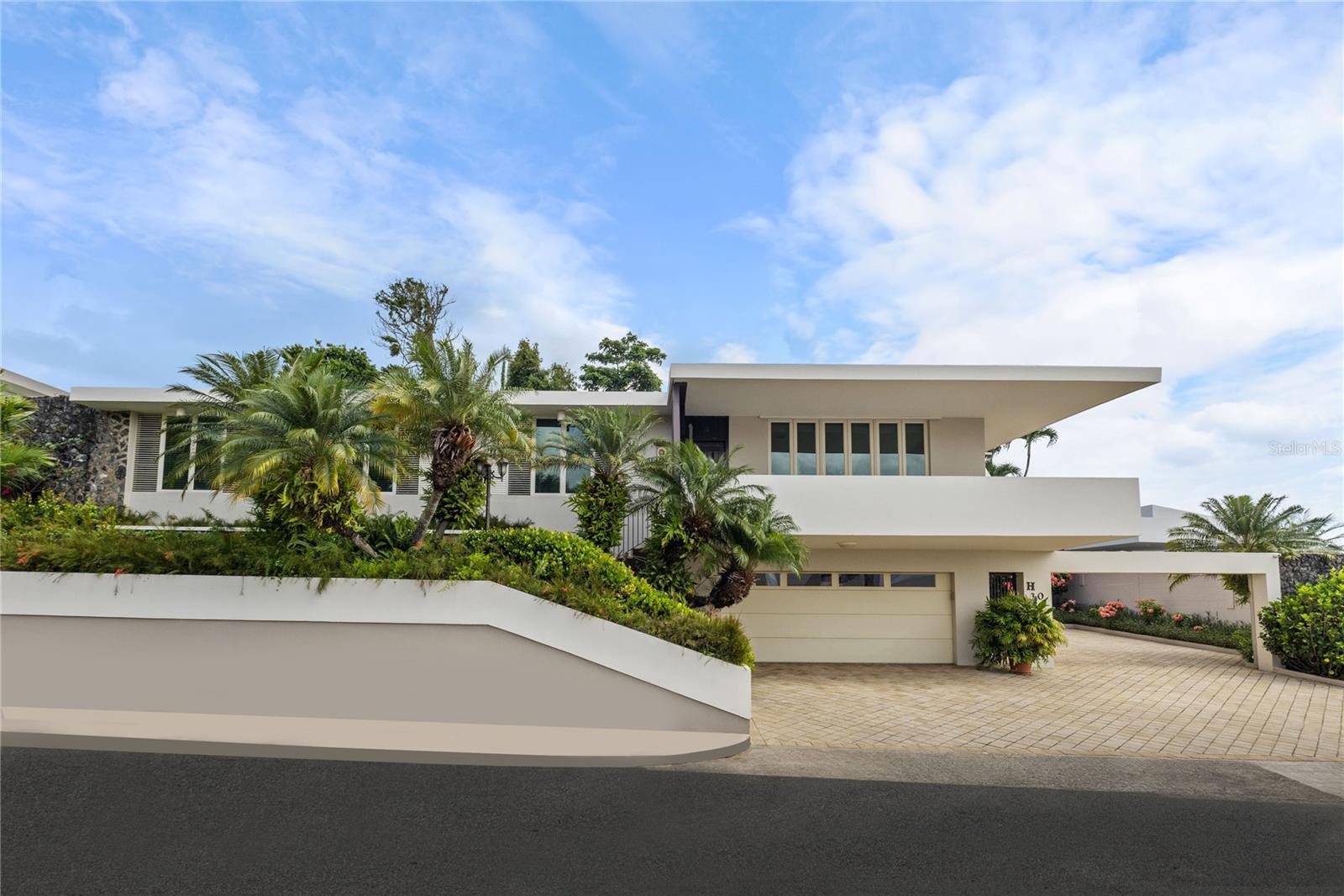 Experience serenity in this elegant home, perched on a small hill in Villa Caparra, Guaynabo, offering stunning city views of Guaynabo and San Juan. Enjoy the privacy of this residence and the refreshing breeze from the trade winds. Located in a gated and secure community with easy access through multiple entry points, this house is an ideal retreat.
The property features a beautiful terrace overlooking a patio with a stone-covered wall, where all stones have been reclaimed from the original construction. The garden includes a charming fountain, several fruit trees, and a swimming pool area complete with a full bathroom.
Inside, the home boasts pristine terrazzo floors with bronze inlays, high ceilings, and large windows that bathe the space in natural light. The spacious kitchen offers a view of the patio and is accompanied by a separate laundry room and maid’s quarters. Among the seven bedrooms and six bathrooms, a separate level includes a bedroom that could serve as a guest room, plus an office.
The house encompasses 3,991 square feet of living space and sits on 1,993 square meters of land. Full back up 30 kilos generator, water tank, solar water heater and much more completes this classic and special house.