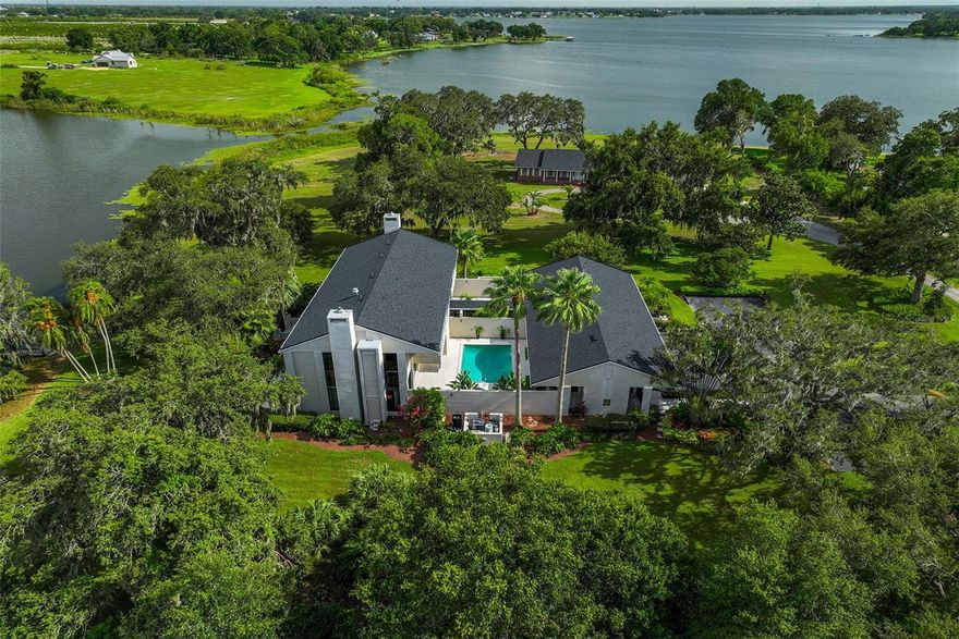 "Eagle Lake" Lakefront Modern 2 Story Estate Home located in Winter Haven Florida! Stunning Waterfront Views~The globally recognized Architect Gene Leedy, the founding Father of the "Sarasota School" of Architecture designed this Masterpiece Modern Home! The exquisite Main House includes 5 Bedrooms plus a Bonus Room and 4 1/2 Baths plus a full Pool Bath. The Guest House offers detached living quarters from the Main House and features 1 Bedroom 1 Bath with a Great Room open floor plan with full kitchen. As you approach the entry of the Main House you feel the grandness of this special Residence with 21+ foot ceilings at the foyer and an 8 foot front door. This spacious home has a wonderful floor plan to include a Formal Living Room with a majestic wood burning fireplace, hand scraped maple wood flooring, custom built-in cabinetry, floor to ceiling windows and doors overlooking the gorgeous waterfront views! The Formal Dining Room features a built-in bar & a massive walk-in pantry, 2nd refrigerator, wine refrigerator, custom built-in shelving & stunning views of the lake~ The open kitchen is perfect for entertaining with pass through windows to the sparkling courtyard pools or the backyard lanai overlooking the massive sized lake. The open kitchen includes Custom Built Wood Cabinetry, Granite Countertops, Pantry with pull out drawers, Stainless Appliances to include KitchenAid Double Ovens, Glass Stovetop, French Door Refrigerator & D/W. The kitchen opens up to the generous sized Family Room with another Wood Burning Fireplace.The Family Room features soaring ceilings, Zebra Bamboo Flooring, a Spiral Staircase & views of the courtyard pool and inviting lake. (there is a 2nd set of stairs leading to the 2nd floor and a possible area to add an elevator) Just off the Bonus Room is a Laundry Station with a Granite Countertop folding station  and a coffee bar with beverage refrigerator, granite countertops & glass tiled backsplash. The 2nd Floor Master Suite is private and separate from the other 4 bedrooms & Bonus Room. The Master Bedroom also has amazing views of the lake, a wood burning fireplace and an enormous walk-in closet with custom closet organizers! The newly renovated Master Bath is impressive & features Marble Tile Flooring & Marble Tiled Shower with Frameless Glass Shower Door, 2 Rain Shower Heads & Wand Shower Head, a dressing table, Bidet, 2 vanity sinks & a large soaking tub with an electric crystal fireplace~The Guest House is truly private and separate from the Main House & offers gorgeous views of the Zen-like courtyard with a fountain. Additional upgrades/improvements include newer roof, newly finished driveway, outdoor lighting, keyless entry, 2 bidets, "Paradise" Propane Gas Grill Outdoor Cooking Station with Granite Countertops, Grill, 2 burners & refrigerator, 2 washer/dryer hookups, outdoor Sonos Speaker and so much more! Inviting heated pool in the cozy courtyard along with a second pool perfectly sized pool for the little ones. (2 feet deep 2nd pool) 3 Car Garages with loads of storage. Oversized lot just under 1.5 acres! Enjoy the Ski-sized Lake Eagle with 628 acres of waterfront to enjoy. Private Covered Dock with swing plus a floating dock too~ No Flood Insurance Required! Enjoy the photos and video of this Sui Generis Masterwork reigning on just under 1.5 acres of paradise! Adjacent Vacant Lot nearly 1/2 acres available at separate pricing~ Furniture and accessories available at separate pricing too!
