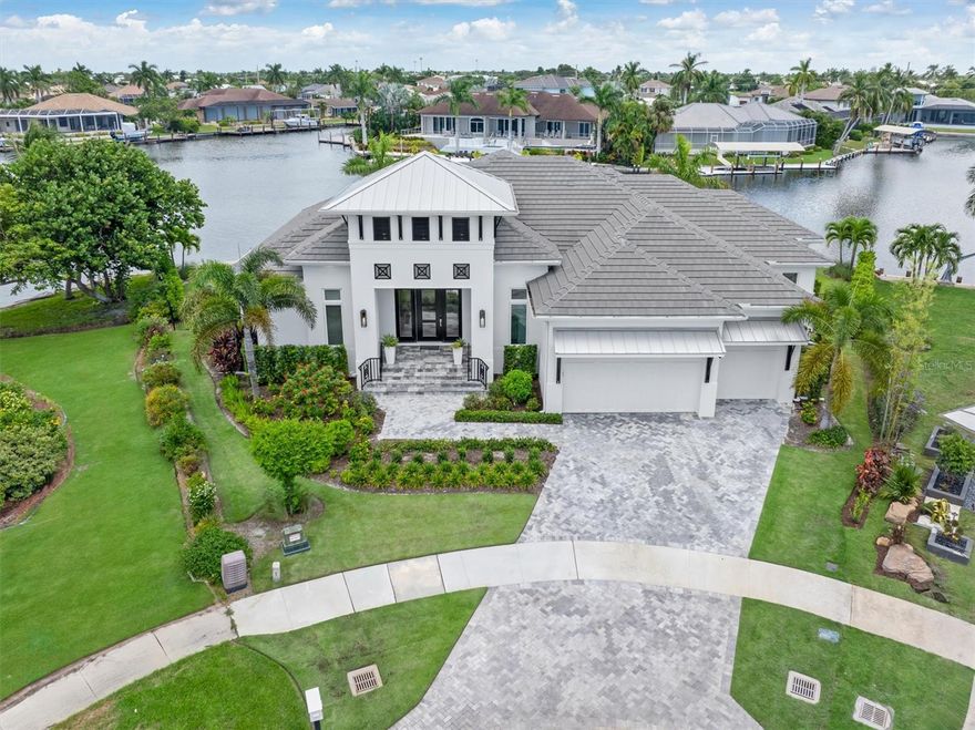 Discover your dream waterfront oasis in this stunning, newly built home on a spacious tip lot with 166 feet of frontage. Surrounded by tropical landscaping, the property boasts a brand-new seawall that spans the entire waterfront. The back of the home features 10-foot impact sliders, offering breathtaking water views and filling the space with natural light. Beautiful hardwood floors throughout the living areas and bedrooms add warmth and elegance. The open-concept kitchen and dining area is a culinary delight, showcasing luxurious quartz countertops and backsplash that perfectly complement the large island with seating for four. Outfitted with top-of-the-line Subzero-Wolf appliances, including a gas range, dual Asko dishwashers, and an oversized refrigerator, this kitchen caters to the most discerning chefs. Additional highlights include instant hot water, a touchless faucet, a pot filler, and a two-zone wine refrigerator in the pantry. The primary suite is magnificent with private sliders to the lanai, where you can relax and enjoy stunning water views. The spa-inspired en-suite bath features dual vanities, a luxurious walk-in shower with dual showerheads, a soaking tub, and an outdoor shower. Two additional guest bedrooms, both with en-suite bathrooms and large walk-in closets, provide ample space for family and guests. A versatile den/office space with lanai access can easily be used as a fourth bedroom if desired. Outdoor living reaches new heights on the expansive lanai, where you can watch manatees and dolphins play in the canal. The covered area with picturesque water views and a motorized privacy screen is perfect for ultimate relaxation. The outdoor oasis continues with a pool, spa, outdoor grill, and seating area overlooking the serene waters. For boating enthusiasts, a new 998-SF Azek dock includes a 7,000-lb lift for jet skis, a 14,000-lb boat lift, plumbing with two faucets and a fish cleaning station. This home is packed with upgrades, including an app-controlled pool and spa system, LED perimeter lighting, and a Sonos speaker system. A three-car garage with epoxy floors offers ample storage, while a 500-lb underground propane tank fuels the pool heater, stovetop, grill, dryer and hot water. With too many features to list, this property truly embodies the essence of luxury waterfront living—you must see it to believe it!