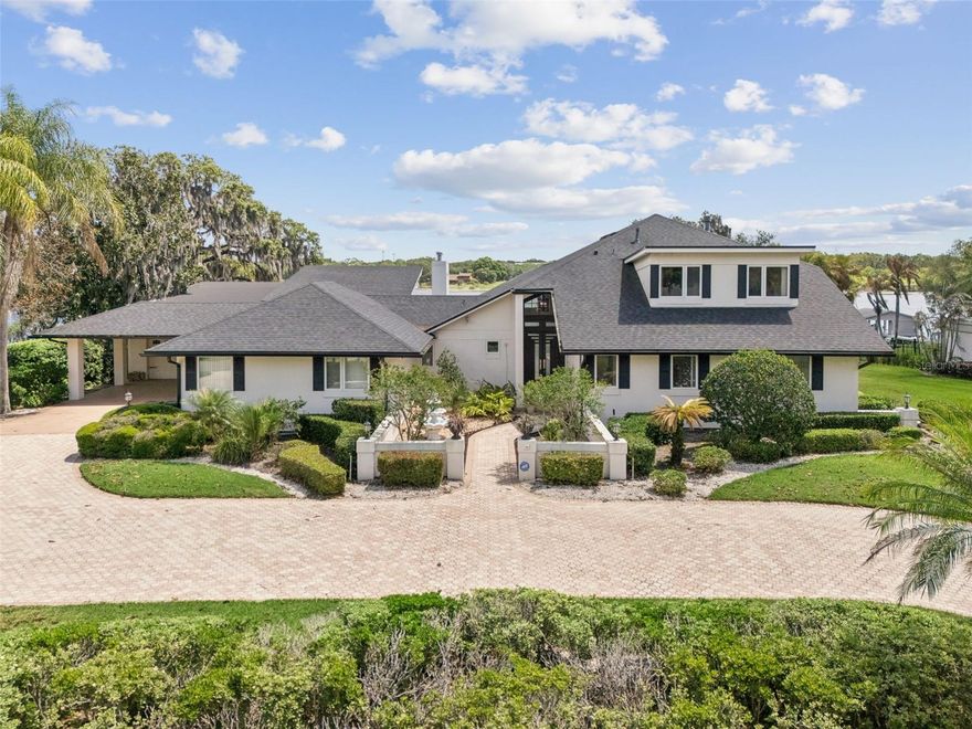 Lakefront estate on Lake Down in the Butler Chain of Lakes with over 150 feet of frontage and no HOA in Sunset Bay. Built in 1983, this 5 bedroom, 4 bath pool home offers nearly 7,000 square feet across three levels and presents a rare opportunity to renovate a true chain-of-lakes property to your own style and standards. Home retains much of its original character and is priced accordingly, creating strong value for buyers seeking premier waterfront frontage, square footage, and long-term upside in one of Windermere’s most desirable locations. Main level includes kitchen, dining area, secondary bedrooms, full baths, oversized laundry room, and sliding doors opening to covered outdoor living and lake views. A few steps down, the sunken living room features a bar, fireplace, storage, and direct water views. Upstairs, the primary suite includes a fireplace, large walk-in closet, dual vanities, tub, separate shower, and screened balcony overlooking the lake. This level also includes a private office. The lower level is a standout feature, offering a full basement living space with its own kitchen, living room, bedroom, full bath, and direct pool access, ideal for extended family, guests, or multigenerational living. An additional reinforced interior room provides flexible use as a secure safe room, storm shelter, private storage room, or secluded flex space. Outdoor features include a screened pool, covered entertaining area, fenced yard, and private dock with space for two boats and two jet skis. Garage space accommodates up to 6 cars, plus a 2-car carport and a large circular driveway that provides additional parking for guests, larger households, or recreational vehicles. Additional storage areas and the lower-level garage create excellent space for boat gear, kayaks, paddle boards, trailers, and lakefront equipment. Home is priced in line with its recent appraisal, with the value reflecting both its current condition and the renovation investment a future owner may choose to make. For buyers seeking a large lakefront footprint, multigenerational layout, extensive parking, and the ability to modernize to today’s standards, this property offers a rare value on the Butler Chain. Located minutes from downtown Windermere, Restaurant Row, golf, shopping, and major attractions.