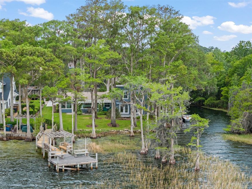 Nestled in the Cypress trees on the northern tip of a secluded Peninsula on Lake Sheen, yet within the gated community of Lake Sheen Reserve, Pineapple Pointe on Lake Cottage Lane exudes character while providing the ultimate private butler chain getaway.  Reminiscent of a bygone era where the lakehouse experience meant a quiet sense of peace, Pineapple Pointe offers stunning water views and a natural escape onto the pristine Butler Chain of Lakes like no other.  Enjoy the waves lapping against the Cypress adorned sandy shoreline and the long views across stunning Lake Sheen, shimmering in the sun.  the quiet canal wraps around the property from the lake, offering a safe harbor from the larger waters, ideal for the boathouse and mooring.  Imagine 280 feet of waterfront at the tip of the peninsula!  A true cottage, the three bedroom, two-bath home features warm finishes and charm throughout.  Off the kitchen, the cozy family room, complete with fireplace, leads to the sunroom, where captivating views of the lake greet.  The living room , dressed with wood plank flooring, opens to the large canal side deck amongst the trees.  Two additional bedrooms, a bathroom, and a study complete the main floor.  The master suite comprises the entire upstairs, with sweeping lake views through the trees, and a large en suite bathroom. 
A new brick paver driveway/parking area has just been completed–other recent improvements include new roof (2026), 21 new windows (2018), and new AC (2022).  Lake Cottage Lane is a private passage that accesses only four homes, and dates to the days of Butler Chain fish camps in the Windermere Groves.  Residents of Lake Cottage Lane enjoy the privacy and security of the gated community of Lake Sheen Reserve, without the HOA requirement.  This private sanctuary is just minutes from Disney and the many area attractions that Central Florida has to offer, while tucked away as a special paradise on Florida’s most famous and sought after chain of lakes.