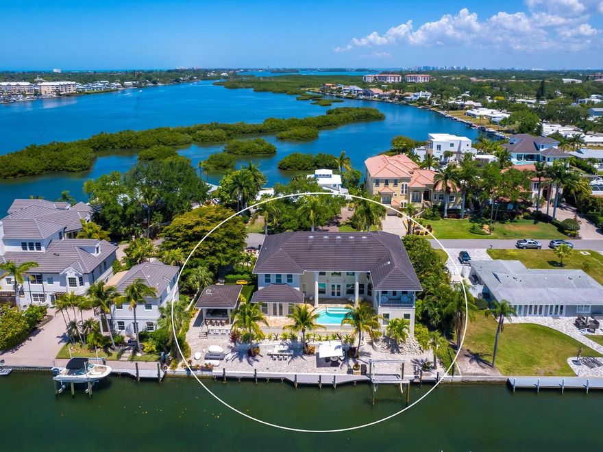 Experience the epitome of waterfront luxury living in this stunning two-story canal-front pool home showcasing a harmonious blend of indoor and outdoor space. This impressive home is a boating enthusiast’s dream located approximately 150’ from Sarasota Bay and minutes to the Gulf of Mexico. Upon arriving at the expanded paver brick circular drive, entering through the glass front double doors prepare to be captivated by soaring ceilings and generous open spaces offering fabulous views of the canal, infinity pool and tropical setting. Elegant touches throughout this custom-built smart home include mahogany flooring throughout, crown molding, plantation shutters, Lutron lighting and a fully integrated Sonos Sound System The expansive living area was made for entertaining, and wine connoisseurs will delight in the glass-front wine closet, together with a separate dry bar, wine refrigerator and serving area. Stepping into the oversized kitchen, cooking enthusiasts will be delighted with two separate islands (one with seating for two), the generous amount of cabinetry and countertop space, the oversized walk-in pantry and high-end appliances.  Extending from the kitchen is the dining area, filled with natural light surrounded by oversized windows and two sets of glass front double doors leading to the outdoor pool area. Meandering back through the living area, enjoy watching movies in style in the media room, which includes a mounted TV with sound bar and beverage fridge.  Continuing on the first level, the expansive Owner’s suite is a luxurious retreat boasting tray ceilings, two walk-in closets, glass front double doors opening to the pool deck, and a large en-suite bath with walk-in shower, spa tub, dual vanities, and water closet with bidet. From the main living area, a beautiful wooden staircase leads to the second level, where three ensuite guest rooms await, one of which features a balcony overlooking the canal and pool area. A fourth guest room (currently used as a workout room), an office, and a separate half-bath complete the second level. The rooms are connected by a beautiful walkway offering captivating outdoor views.  Winding back downstairs, the outside living area combines three levels of canal and bay vistas. The first level opens from the living, kitchen and dining area, onto a large travertine deck, with heated infinity pool and spa overlooking the canal. The lower level deck boasts a 16K lb sling boat lift, newer dock area with water, electricity, and plentiful space along the paver deck for dining, casual seating and enjoying the oblong gas firepit. The second deck level promotes entertaining in style with the stand-alone summer kitchen featuring bar seating, double drawer refrigeration, beverage fridge, ice maker, dishwasher, gas grill, burner, sink, pizza oven and a drop-down TV to complete your outdoor oasis.  Nestled on the north side of the summer kitchen is an area filled with astro-turf, surrounded by lush landscaping and a fence leading to the front drive. Additional features of this home include an interior laundry room on the first level, an expanded two-car garage with additional storage, and two exterior storage sheds. This home is ideally located moments away from Siesta Key and it's world-renowned beaches, and within close proximity to downtown Sarasota, incredible shopping and dining, and myriad cultural attractions. Experience serene and seamless indoor/outdoor living in this stunning waterfront oasis.