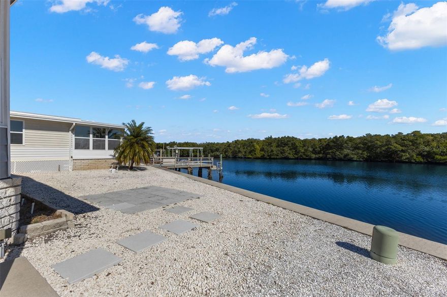 This 1,600 sq. ft. waterfront home offers 2 bedrooms and 2 bathrooms and is ideally situated on a wide canal with quick, bridge-free access to Tampa Bay. Custom built in 1990, the home features cathedral ceilings, luxury vinyl plank flooring, expansive windows, and sliding glass doors that capture beautiful water views. Two separate living areas make entertaining effortless. Recent 2024 upgrades include a new HVAC system, new roof, and a structurally engineered carport. The kitchen is appointed with granite countertops, tile backsplash, a built-in oven plus a range/oven, a functional island offering seating and additional storage, plus a convenient pass-through to the living area. Both bedrooms are generously sized with spacious walk-in closets. The primary suite includes an ensuite bathroom with a large walk-in shower, while the guest bathroom features a bathtub. Additional highlights include an interior laundry room and ceiling fans throughout. The community-maintained seawall is a valuable benefit. Dock and lift may be added for the boating enthusiasts, or just enjoy the breathtaking views from your home or backyard! Home is located in Americana Cove. Price includes share for the lot and ownership in the co-op. 2 pets (dogs or cats) up to 35 pounds are welcomed. Low monthly maintenance fee of $380 includes water/sewer, trash pick up, lawn mowing, 24 hr manned gate, private streets and all amenities including clubhouse, fitness center, heated pool, billiards and so much more! Location is excellent: only 10 mins to downtown St. Petersburg, 5 mins to 4th Street shopping, dining and grocery, and 20 mins to two airports.