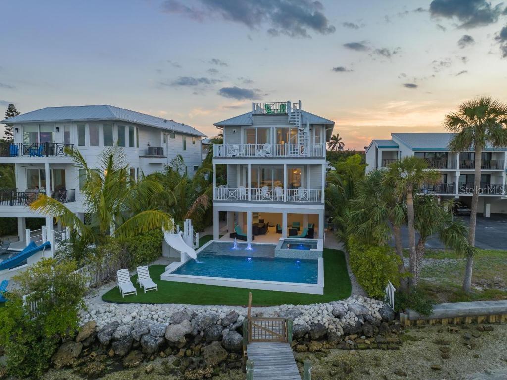 VIEWS, VIEWS AND MORE VIEWS!!! Positioned directly on the sparkling waters of the bay in Bradenton Beach on Anna Maria Island, this extraordinary coastal estate offers over 4,000 square feet of luxury waterfront living. With five spacious bedrooms and five and a half baths, this home captures the essence of island elegance while delivering high-end comfort and resort-style amenities. It is truly a rare opportunity to own one of the island’s premier bayfront properties, complete with sweeping water views, a private dock, and incredible rooftop panoramas of both the Gulf of Mexico and the bay.This home makes a stunning impression from the moment you arrive. The tropical landscaping and striking architecture immediately convey a sense of vacation-ready serenity. Inside, the open-concept design is beautifully finished with coastal accents and abundant natural light that floods in from floor-to-ceiling glass. The expansive main living space seamlessly flows from a gourmet kitchen outfitted with stunning counters and custom cabinetry to a water-view dining area and elegant lounge, all opening out to deep covered balconies. Each bedroom is thoughtfully designed with comfort and privacy in mind, many with their own ensuite baths and outdoor access. The owner’s suite is a serene waterfront haven with its own balcony and a spa-style bathroom featuring dual vanities, a soaking tub, and a walk-in shower. Every detail of this home is designed to highlight the stunning surroundings and to provide maximum comfort for everyday living or short-term vacation stays. Step outside to a private paradise that feels like your own resort. A sun shelf and water slide pour into the sparkling bayfront pool, while the adjoining spa is perfect for soaking under the stars. The lush lawn, poolside lounge areas, and waterfront dock provide endless opportunities for relaxing or entertaining. An outdoor spiral staircase leads to a rooftop balcony with unobstructed panoramic views stretching from the Gulf to the bay—one of the best sunset spots on the island.
Located just a short stroll or golf cart ride from the beach, shops, and restaurants of Anna Maria Island, this property offers the best of both waterfront tranquility and island activity. It also operates as a successful vacation rental, offering excellent income potential for investors seeking a blend of luxury and performance. Whether you’re watching dolphins swim past the dock, enjoying rooftop cocktails at sunset, or taking a dip in the pool with the bay as your backdrop, this home delivers the ultimate in coastal lifestyle.
