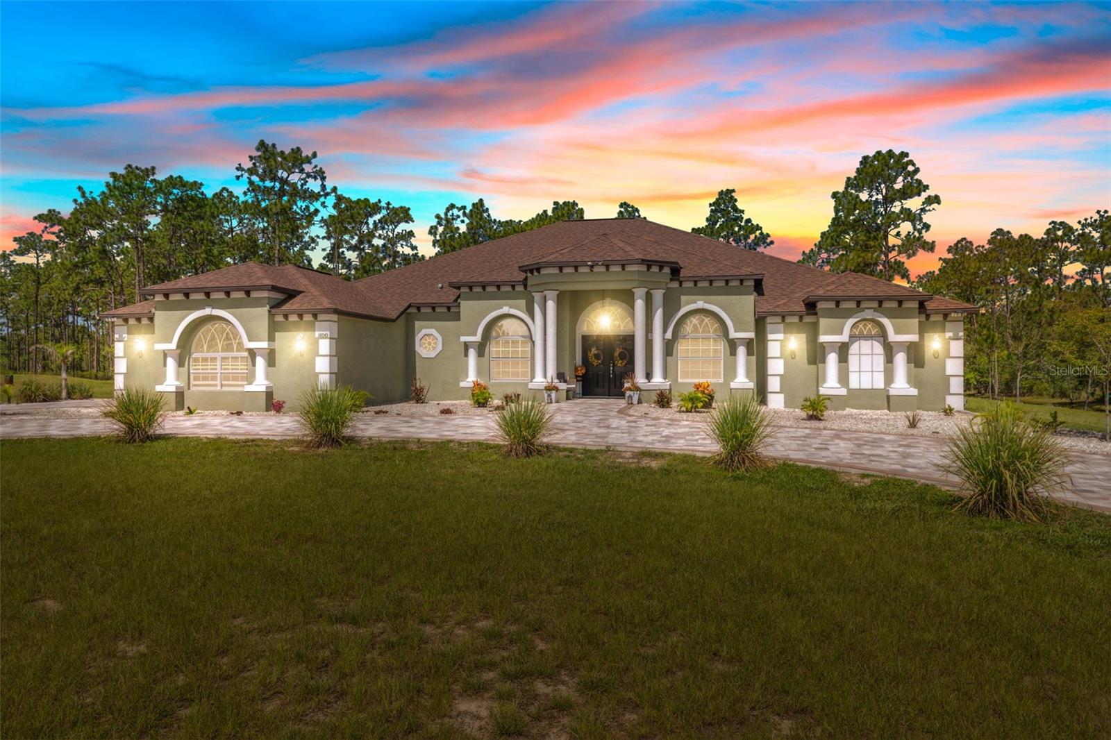 Custom-built 4-bedroom, 3-bathroom home situated on 1.2 acres in Royal Highlands. Built in 2023 by Dream Custom Homes (Don Valencia model), this single-story residence offers 3,528 square feet of living space and 4,775 total square feet under roof. Located at the end of a dead-end street, the property provides privacy and a cleared, landscaped lot with no HOA or CDD.
A 5,000 sq ft paved driveway leads to a 3-car garage and was completed with a high estimated value. The rear of the property offers a covered lanai with dual seating areas, wooded views, and a designated fire pit area. Electrical infrastructure is in place for a future pool.
Interior features include tray ceilings, tile and luxury vinyl flooring throughout, and an open-concept layout with formal living and family rooms. A marble-style accent wall surrounds the electric fireplace in the main living area. The kitchen includes granite countertops, espresso cabinetry, walk-in pantry, and a large island with breakfast bar seating. All kitchen appliances are stainless steel and include smart technology.
The primary suite features a private sitting area with bay windows and column accents, two walk-in closets, and an en-suite bath with a garden tub, dual-entry walk-in shower, and dual vanities. A split-bedroom floor plan includes three additional bedrooms and two full bathrooms. A flex room is currently used as a home gym.
Additional features include a spacious laundry room with upper shelving, utility sink, and cabinet storage. The property also includes six exterior security cameras with recording capabilities. Well and septic. Flood Zone X. Zoned R1C. Paved road with public maintenance.
Located near US-19 and State Road 50 with access to local schools, shopping, and medical services.