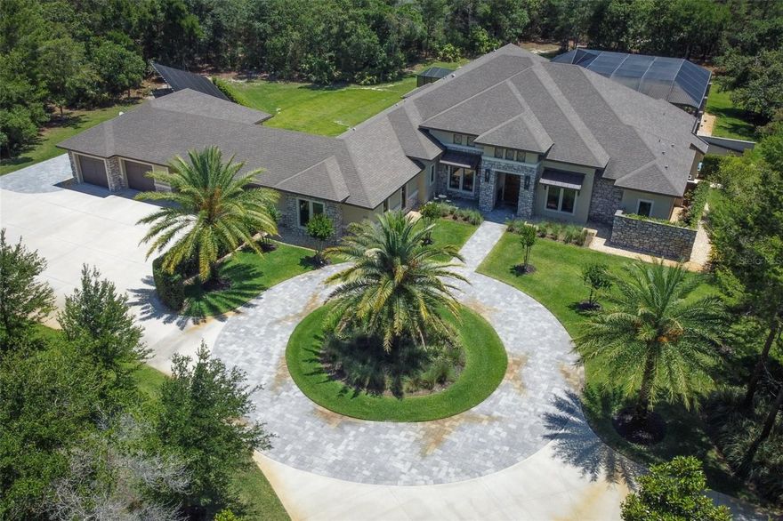 This stunning 4800+ single level estate, with a 5 car garage, located behind the gates of Seminole Woods in Geneva can now be yours! Enjoy the scenery of rural Florida landscape, while providing privacy for your compound. The extended, circular driveway feature eases the parking & traffic flow, leading you to the statement piece custom pivot swing door. This home design is perfect for entertaining with its open layout inclusive of the dining room, dedicated wine room, wet bar w/ frig & plumbing for ice maker, family room, kitchen & cafe area. Details include: 72 inch linear electric fireplace w/ multi color flame features, accent shelving & lighting, coffered ceilings throughout & more. The gourmet kitchen boasts an expansive single level center island, induction range with a pot filler, double built-in ovens, large farm sink, closet pantry, & hidden walk-in pantry with an additional refrigerator is a chef's dream. Conveniently located to the right of the foyer is the home office/flex room to adapt to the evolving needs of every household. The primary retreat is luxurious, with its spacious sitting area overlooking the pool and patio and two walk-in closets. The primary bath has a private garden view, large walk-in shower with 3 shower heads, large vanity with dual sinks and makeup vanity, toilet with bidet, and walk-in spa tub is the perfect place to unwind. The wing off the kitchen, tucked behind the dining room, holds 2 of the secondary bedrooms, separated, shared bathroom, the laundry room & entry to the garage. The wing off the kitchen cafe area holds the remaining secondary bedroom, hall bathroom & media room. The media room showcases triple sliding pocket doors that open up to the pool and lanai area, exposing the amazing outdoor entertainment space. A 5th bedroom/attached casita is located within the roofline of the lanai and functions as a fabulous guest suite with a full bath and walk-in closet. The pool/spa/patio/outdoor kitchen area with its saltwater infinity pool heated by solar, heat pump or propane, and controlled by a Hayward Omni Logic control system, and the heated spa with lounge chairs provides your own resort-like space to enjoy. In addition to the 2-car garage that is part of the main home, a connecting porte cochere provides covered parking for multiple vehicles, while connecting the building hosting the additional 3 car garage with a workshop. This area includes TESLA 80 amp charging station, RV hookup, attic storage, and connecting porte cochere and outdoor parking space, as well as the new RV parking pad, making for convenient parking options. Additional features include: electric window shades, crown molding, 10 and 12 ft. ceilings, bluetooth enabled ceiling fans, 3 AC units, 2 NEW septic systems, 2 propane tanks, whole house sound system, security system, massive attic storage with lights and a catwalk bridge, deep well irrigation system, landscape lighting and tankless water heaters. The whole home solar array system, located behind the garage, keeps the electric bills in the range of $100 monthly. Seminole Woods offers privacy & convenience behind a staffed security guard gate, dual entrances/exits & contained amenities. Explore miles of equestrian trails, a centralized 12- acre private lake park that provides party pavilions, bathroom facilities, playground, beach area, boat launch & dock on the 159 acre Buck Lake for water sports/activities & basketball courts.