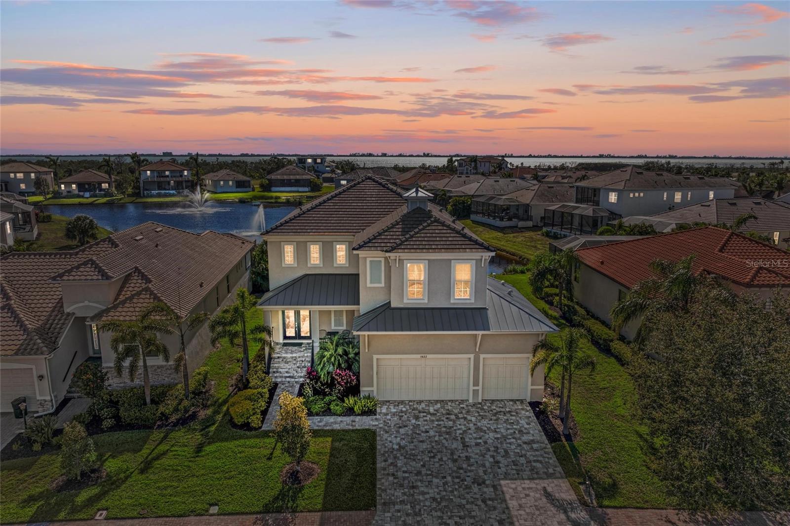 Beautiful inside and outside, this luxurious coastal contemporary home in Legends Bay is a must-see for those seeking a spacious retreat in a prime location. Nestled along the bay in a picturesque, gated neighborhood, this immaculate, storm-safe home is in excellent condition. Situated on a quaint homesite with sparkling water views, this serene sanctuary is ready to be enjoyed. Soaring ceilings give way to an elegant great room centered around a showcase gourmet kitchen with fabulous entertaining space, stainless-steel appliances, and gleaming quartz counters. The indoor area flows seamlessly to the outdoor area with a gorgeous saltwater heated pool, spa, outdoor kitchen, and covered lanai. A guest suite downstairs offers convenience for a bedroom or office. Upstairs, the well-appointed primary bedroom offers sweeping views, double walk-in closets, a walk-in shower and soaking tub, and glorious sunlight. The adjoining loft offers space to unwind and a second-story terrace with dreamy views. Three additional guest rooms provide privacy for family or friends. Impact windows and sliding glass doors provide safety and lower insurance premiums. This spectacular energy-efficient home shows like new and is move-in ready. Legends Bay is a gated enclave with a community clubhouse, swimming pool, walking paths, a lakeside fishing pier, and is golf cart accessible to IMG. This exceptional quality-built home has had no storm damage and offers lower insurance premiums based on the elevated stem wall foundation and quality construction features. The HOA covers yard maintenance and cable/internet. Come see this incredible residence!