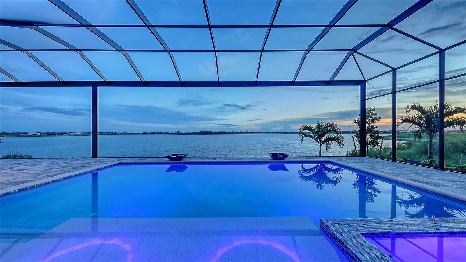 Enjoy spectacular ‘Big Lake’ Views from this Brand-New Luxury Home in Wild Blue at Waterside. Step into refined elegance with this expansive, never-lived-in home—just one month new—boasting over 4,200 square feet of luxury living on a rarely available oversized homesite. Perfectly positioned to capture panoramic lake views, this 4-bedroom/4.5 Bath home includes a dedicated office and an exercise room, all designed around a wide-open floorplan that effortlessly blends indoor and outdoor living. From the moment you arrive, the home’s impressive curb appeal stands out, featuring a paver driveway, a split 4-car garage, and a grand foyer entry with hardwood flooring that opens to a soaring decorative recessed ceiling with a stunning lakeview. Inside, custom architectural details abound, including a spectacular floor-to-ceiling ledgestone wall with a linear fireplace and custom built-in shelving and cabinets with underlighting that anchors the great room in modern sophistication. The gourmet kitchen is a chef’s dream, featuring a striking combination of stained and painted cabinetry, Skara Brae quartz countertops, a massive island, and top-of-the-line professional paneled appliances. Designed for both everyday comfort and sophisticated entertaining, the expansive great room opens directly to your private resort-style oasis with pocket sliding glass doors. The primary suite occupies its own private wing with two custom walk-in closets and a spa-like bathroom, with split vanities, and offering ultimate luxury and convenience. Step outside to your personal retreat—an entertainer’s paradise, complete with a luxurious pool and spa with sun shelf, a shaded covered lanai with a linear fireplace, and a fully outfitted summer kitchen ideal for alfresco dining and gatherings. Wild Blue delivers an unparalleled lifestyle in the heart of Lakewood Ranch, offering a rich array of world-class amenities. Outdoor enthusiasts will love the scenic walking trails, yoga lawn, and putting green, while sports lovers can take full advantage of the Midway Sports Complex—featuring eight pickleball courts, six tennis courts, and a professional-grade pro shop. The community also includes a dog park and playground, catering to every member of the family. The resort-style clubhouse is currently under construction and will feature concierge service, a private theater, state-of-the-art fitness studio, golf simulator, billiards room, and an expansive pool complex with not one but two resort-style pools. A full-service restaurant and patio bar are coming soon, elevating the social experience even further. Wild Blue is ideally located near The Mall at UTC, Lakewood Ranch Main Street, Waterside Place, and some of the area's top dining and shopping destinations, Wild Blue represents the pinnacle of luxury living in this Lakewood Ranch multi-generational community.