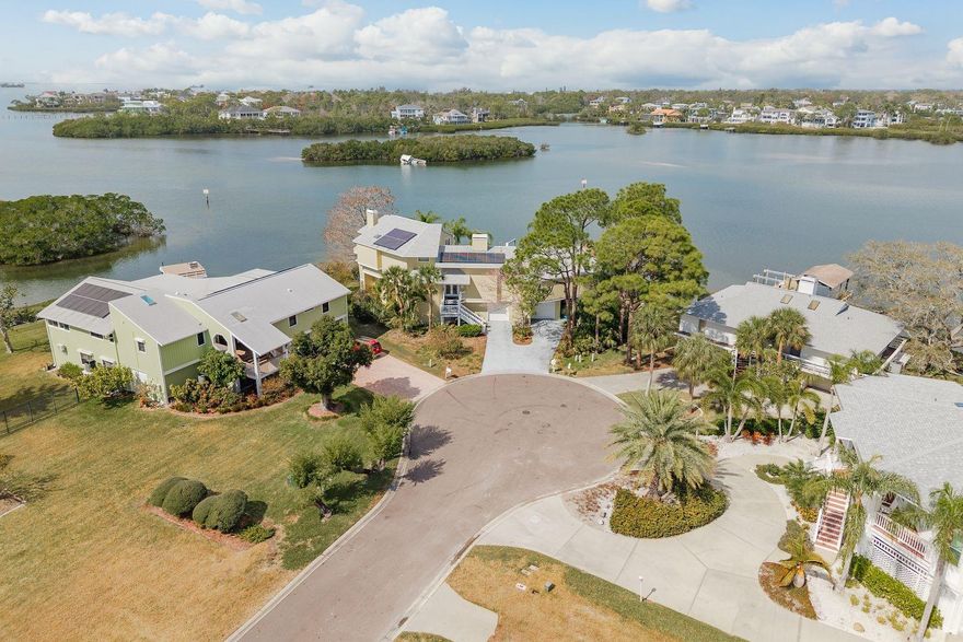 Welcome to the ultimate boatable waterfront retreat offering unparalleled views of Southerland Bayou at the entrance to the Intracoastal Waterway. Perfectly positioned in the highly sought-after Ozona community, this exceptional residence rests on a quiet cul-de-sac, providing breathtaking panoramic water vistas. This stunning Key West–style home makes a warm first impression with its charming white and yellow façade and eco-friendly solar power. Ascend to the elevated main level where endless water views immediately captivate. The expansive open-concept features soaring two-story ceilings and a cozy wood-burning fireplace. The rear of the home offers 180-degree water views and opens onto a wraparound covered porch. Below, enjoy a sparkling pool and lanai and private dock and covered boat lift. With deep, boatable water, this property is truly a boater’s paradise. Back inside, the main level is designed for entertaining. A spacious bar area flows into the oversized kitchen, complete with granite countertops, stainless steel appliances, custom wood cabinetry and a breakfast bar overlooking the breathtaking views. Adjacent is a formal dining room featuring intricate ceiling detailing and sweeping water vistas. An additional office/bedroom/in-law suite includes built-in bookshelves and an attached half bath with potential to convert to a full bath. A closet pantry, separate laundry room and an electric dumbwaiter add convenience and functionality. On the opposite wing, two generously sized guest bedrooms offer sliding door access to the lanai and share a Jack-and-Jill bathroom with dual vanities and granite countertops. An additional guest bath completes the level. There is also a spacious OFFICE/5TH BEDROOM on this level with another bathroom!! Up the grand open staircase, discover the luxurious primary retreat. A versatile bonus room off the landing ideal for an office, nursery, or additional closet precedes the spacious primary suite with soaring wood ceilings. Additional features to this primary bedroom include a hobby room or huge walk-in closet and a beautifully appointed en-suite bath with an oversized soaking tub, seamless glass walk-in shower, double vanities, private water closet, and another custom walk-in closet with built-in organization. A charming sitting room with a gas fireplace and vaulted ceilings adds warmth and character. Take in spectacular water views through custom plantation shutters or step onto your private covered balcony for morning coffee and coastal breezes. The ground level offers an opportunity for an in-law suite with a full pool-access bathroom, living room, kitchenette with granite counters, and an additional enclosed flex room recently refurbished ideal for guests or multi-generational living. Two spacious garages, a workshop, and abundant storage complete the space. Notable upgrades include three HVAC systems (2017, 2018, 2020), Roof 2018, a monitored alarm system, two boat docks, and solar power. Situated in a beautifully maintained, HOA-free upscale neighborhood, this home is just minutes from charming downtown Palm Harbor and Crystal Beach, with endless dining, shopping, and award-winning beaches nearby. Tampa International Airport is only a 30-minute drive, along with excellent medical facilities and top-rated schools. This rare waterfront gem offers luxury living, privacy, and direct access to Florida’s premier boating water. Its an extraordinary opportunity to live the ultimate coastal lifestyle.