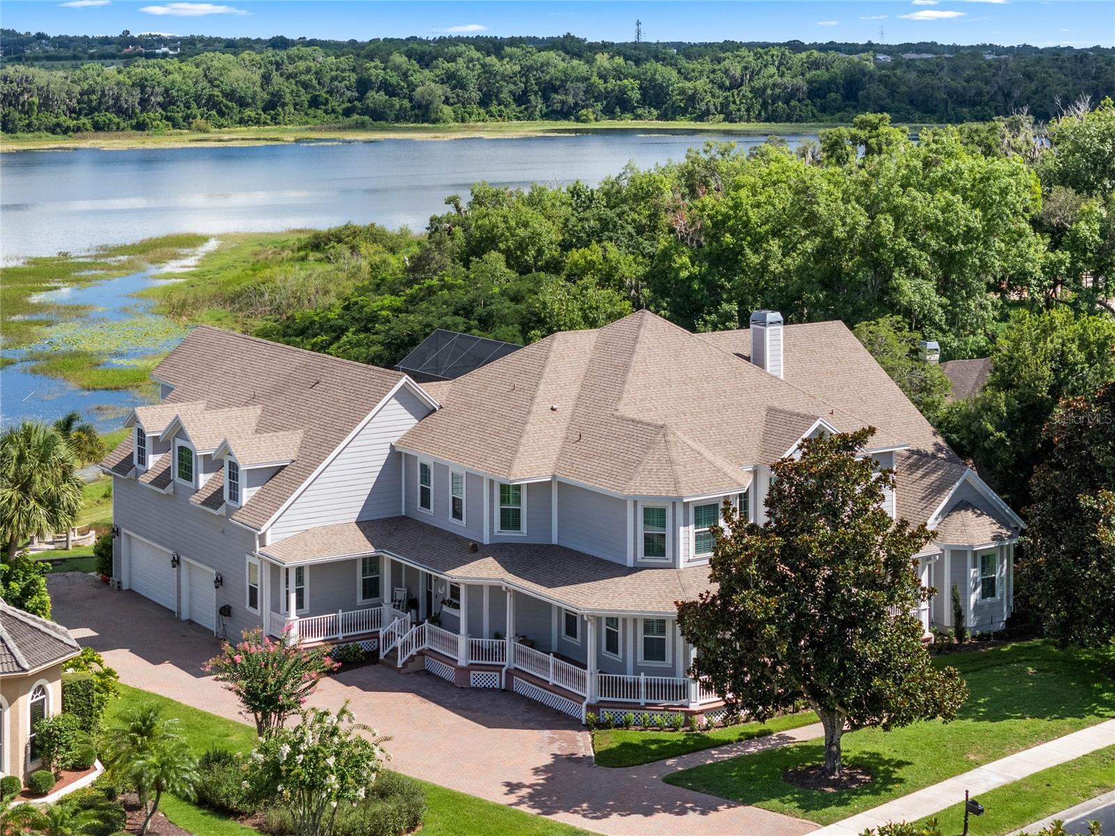 Welcome to your dream home! This stunning lakefront custom family residence is nestled in the serene, guard-gated community of Magnolia Pointe, featuring a separate gated entrance exclusively for the lakefront estates. With 140 feet of pristine lake frontage on the spring-fed Johns Lake, this Victorian-style masterpiece offers 6 bedrooms, 4 full baths, and 2 half baths, spanning an impressive 6,830 SqFt under air. Every night, enjoy a clear view of Disney fireworks from your pool or balconies. Johns Lake is perfect for bass fishing, boating, and water sports. This home underwent a complete renovation in 2019, featuring a new gourmet kitchen with top-of-the-line Thermador appliances, a Uline ice maker, and a bar fridge. Luxurious porcelain tile and engineered hardwood flooring were installed throughout. All bathrooms have been exquisitely remodeled, and the home showcases elegant wainscoting and crown molding. Additional upgrades include new windows, pathway stairs, a fire pit, a resurfaced dock with a 7500# lift, and a new two-story screen enclosure. The pool area boasts new Pentair equipment with gas and electric heaters, and new pavers on the back patio as well as a pool refinish. The outdoor kitchen is a chef's dream, complete with a Lynx pizza oven and Summerlin grill. Interior enhancements feature a sliding glass wall, a resurfaced fireplace, new lighting fixtures and fans, California closets throughout, and a redesigned staircase with hardwood and wrought iron. Plantation shutters adorn the windows, and a custom home office with built-ins, new cabinets, and a redesigned laundry room and pantry add functionality and style. A charming wrap-around porch expanded brick paver driveway, and a 3-car garage greet you upon arrival. The glass front door floods the home with natural light, welcoming you into a grand foyer with wood stairs and risers. The formal dining space, perfect for hosting, seats 10 comfortably. The luxury chef’s kitchen, equipped with top-of-the-line appliances, vent hood, pot filler, farmhouse sink, ice maker, and bar fridge, offers ample storage with high-end cabinets, a huge island, and an enormous fridge. An IT nook with matching counters and cabinets adds convenience. The connected in-law apartment, equipped with Frigidaire Pro appliances, provides an ideal space for extended family or guests. The informal dining area offers picturesque views of the lake, while the expansive family room features vaulted ceilings and sliding glass doors that open to the pool, lanai and outdoor kitchen. The first-floor playroom is ideal for children or as a home gym. The second floor boasts a large private master suite with a sitting area, a screened balcony overlooking the lake, and a spa-like master bath with a spacious shower, double and single vanity sinks, a garden tub, and a custom California closet. Three additional bedrooms, two full baths, a home gym, and a media room/den that can be used as an extra bedroom complete this floor, making it perfect for a growing family. Don't miss the opportunity to own this exquisite lakefront property. Community amenities include tennis courts, a shaded playground, basketball courts, a gazebo, a dock, a boat launch, and a beach. Located near major roadways, shopping, dining, and more, this is a rare opportunity you don’t want to miss. Contact us today to schedule a private tour and make this dream home yours!