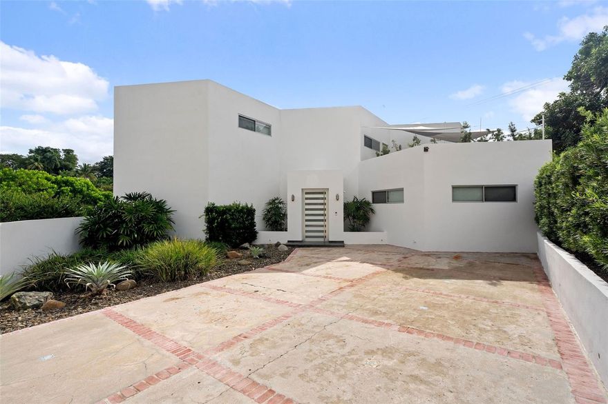 Meticulously remodeled, this unique property boasts modern and functional design, high ceilings, generous dimensions, oversized windows, and natural stone finishes. Intelligent home system & gadget ready, with cat5 video and audio cabling throughout. built-in lighting, speakers, cabinets and closet systems. 7 Individual & 3 Central A/C units, 26KW diesel power generator, 2,000+ Gal freshwater tank, and central water filtration system. Nestled in a quiet cul-de-sac, it is surrounded by lush greenery in one of the most privileged locations, with unmatched privacy, tranquility and easy access. Oversized windows seamlessly blend indoor and outdoor spaces, creating a tranquil retreat that combines modern elegance with natural beauty. complementing clean lines with nature’s palette, overflowing textures and angles. Well-manicured garden with fruit trees, herbs, and a vegetable plot. The first-floor showcases a living room, dining room, large kitchen, office/gym, and a remarkable home theater/entertainment room. The second floor features a grand master bedroom, four additional bedrooms, and a family room/lounge area. Outdoor living is a delight with a pool, poolside bathroom, outdoor shower, grassed area, mature trees, and manicured lawn. The lot is fully enclosed by a concrete wall with patio gates to both the street and an adjacent community park hosting a variety of small-scale private fitness offerings. Santa Maria stands as one of San Juan's most sought-after neighborhoods, offering an unmatched location, with a variety of guarded entrances that facilitate getting around, recreational amenities, proximity to top schools, abundant greenery and serene privacy. Experience the luxury of living in Santa Maria. Contact us today to schedule a private tour and discover this remarkable home.