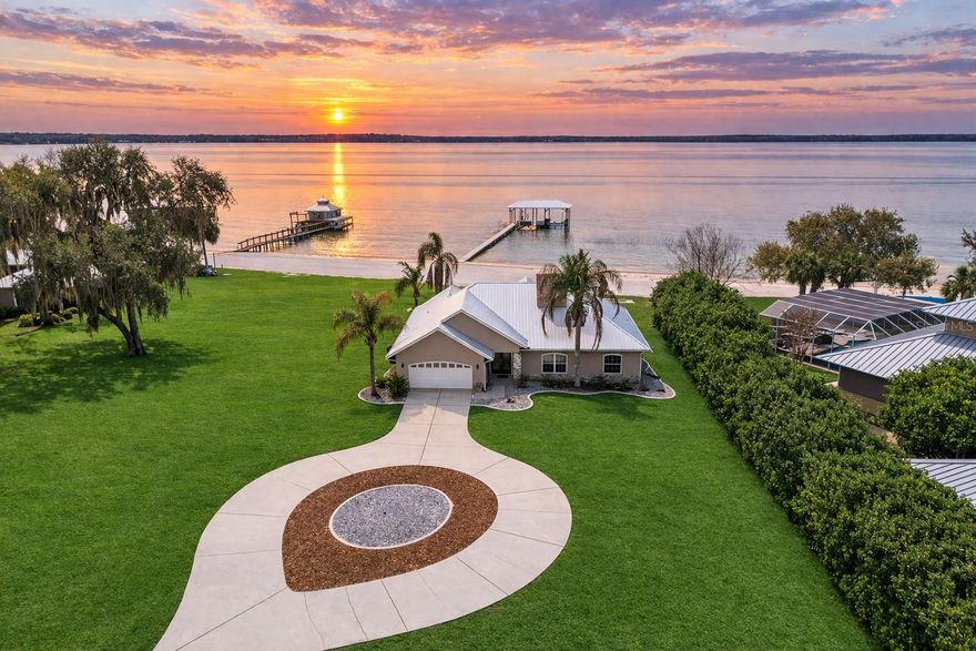 Along the shoreline of Lake Weir in the Sandy Hook area, this lakefront residence offers 200 feet of sandy shoreline, expansive outdoor space and direct access to one of Central Florida’s established recreational lakes. On just over two acres, the property provides privacy, flexibility for outdoor improvements and unobstructed water views. The home faces west across the lake, offering sunset views over the water. The 2,204-square-foot residence includes three bedrooms and two baths with a split floor plan designed for entertaining and everyday living. An open kitchen connects to the main living and family areas, anchored by a double-sided fireplace that links the interior gathering spaces. Large windows and primary living areas frame views of the lake and surrounding landscape. The primary suite includes a walk-in closet and bath with a walk-in shower, garden tub and dual vanities. Two additional bedrooms and a full bath are positioned on opposite side of the residence, providing separation for guests or family members. Additional improvements include a 40-by-36-foot detached building, suitable for equipment storage, workshop space or hobby use, providing flexibility for tools, lake gear or recreational equipment. Outdoor living centers around the lakefront setting. A private dock extends into Lake Weir, providing access for boating, fishing and waterfront recreation. The property’s sandy shoreline and open lake frontage create space for lakeside seating, swimming and water activities. Lake Weir spans approximately 5,600 acres and is known for boating, fishing and swimming. The Sandy Hook area features established homesites and a lakefront setting. The property is also within convenient driving distance of The Villages and Ocala, providing access to shopping, dining, medical services and year-round entertainment.