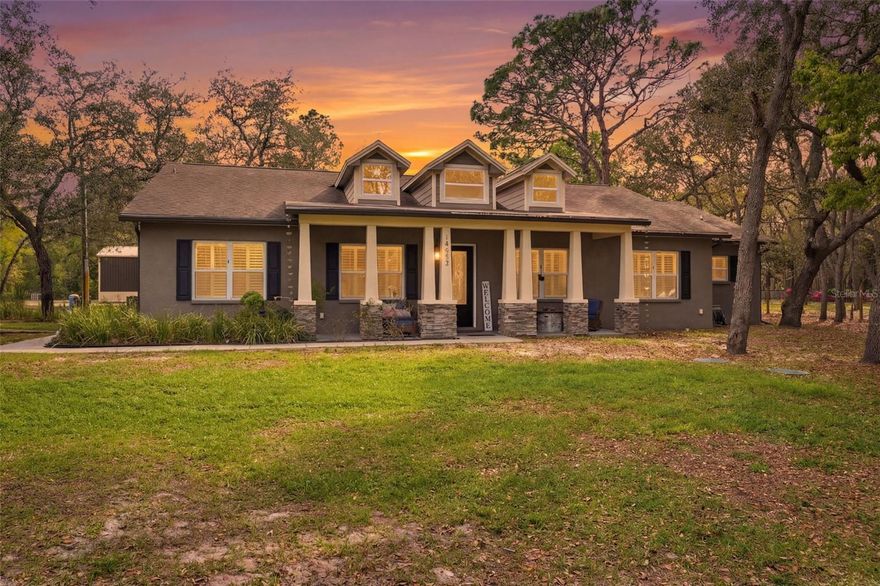 This immaculately maintained, thoughtfully designed home features 4 bedrooms, 3 bathrooms, and 2,842 square feet of living space, along with a detached RV building/garage and spacious outdoor living area, all set on a 1.97-acre lot with a rural feel while remaining close to Hudson. From the moment you arrive, mature trees frame the front lawn, creating a sense of privacy, while a covered front porch extends across the home, offering space for seating and outdoor use. Inside, the foyer opens with porcelain tile flooring throughout, high ceilings, and decorative glass double doors. To the left, the dining area sits beside the kitchen with large front-facing windows, while to the right, a flexible office or den provides additional space with views of the front yard. The central living area connects seamlessly, featuring crown molding and French doors leading to the outdoor space. The kitchen offers porcelain tile flooring, granite countertops, stainless appliances, solid wood cabinetry, recessed and pendant lighting, and opens to the family room and breakfast nook with backyard views. The family room includes a wood-burning fireplace and French door access to the covered rear porch. The primary bedroom is privately located at the rear with porcelain tile flooring, crown molding, outdoor access, and an ensuite bathroom with a soaking tub, walk-in shower, and closet. Three additional bedrooms provide flexibility, including one with a private bathroom suitable for guests. The laundry room includes tile flooring, a sink, and overhead cabinets with access to the side of the home. A walkable attic space with approximately 6-foot height offers storage or potential expansion. The roof, water heater, and AC are approximately seven years old, with additional upgrades including plantation shutters and crown molding throughout. The covered rear porch spans most of the home and overlooks the backyard with raised garden beds, while irrigation zones and gutter guards support outdoor maintenance. A 25x42 concrete pad provides additional outdoor space, and the property includes a well and septic system. The detached 30x40 metal building constructed in 2025 allows RV access with multiple roll-up doors, windows, and electrical setup including 110 and 220 outlets, making it suitable for vehicle storage or workspace. An additional acre remains undeveloped, offering future possibilities. Conveniently located near nature preserves, golf courses, shopping, and dining, with access to major roadways, the home is approximately one hour from Tampa, minutes from Hudson, and within driving distance to Gulf Coast beaches, providing a balance of space, privacy, and accessibility.
