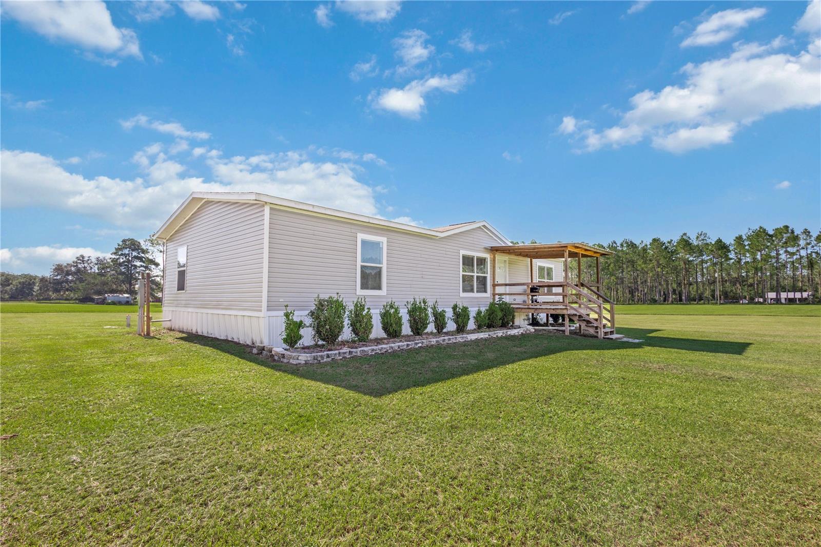 Welcome to this beautifully maintained 3-bedroom, 2-bath double-wide mobile home nestled on 5.14 acres of cleared land in the heart of Williston, FL. Built in 2019, this spacious 1,612 sq ft home features an open floor plan that seamlessly connects the living room, dining area, and kitchen—complete with a central island, walk-in pantry, and dedicated laundry and storage space. The main bedroom offers a private retreat with a walk-in closet, en suite bath featuring dual sinks, a separate shower, and a soaking tub with a serene window view of the property. Both additional bedrooms also feature walk-in closets, providing ample storage throughout the home. Special touches like wood beams in the family room, a cozy foyer, and a newly added porch enhance the home's charm. Outside, you'll find a generous 30x20 carport and a convenient storage shed, offering plenty of space for vehicles, tools, and equipment. This property combines comfort, functionality, and peaceful country living—all just minutes from local amenities and outdoor recreation.