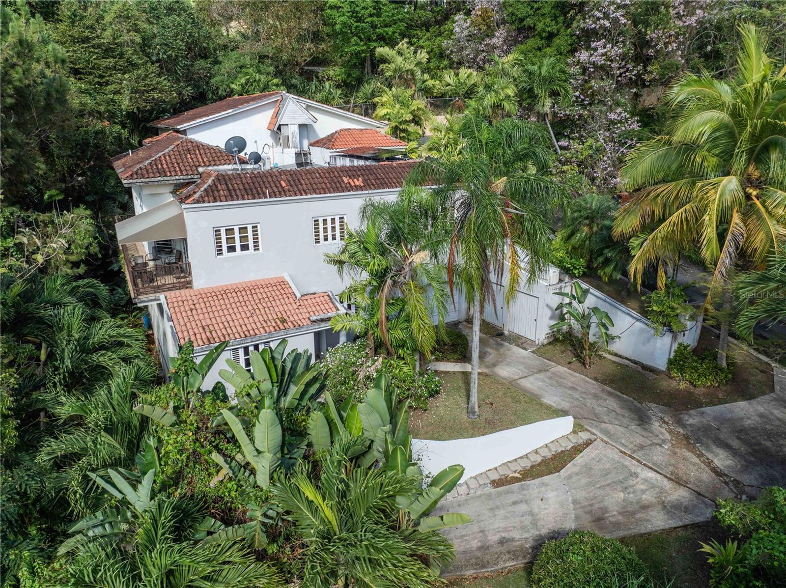 Exclusive 3-Level Home with City View Surrounded by Lush Gardens
Welcome to a rare opportunity in the exclusive Urbanización La Lomita in Guaynabo. This expansive 6,011 sq. ft. residence offers three thoughtfully designed levels, ideal for multi-generational living or creative reimagining into a grand single-family estate. The main upper level features soaring cathedral ceilings, a spacious living room, dining room, family room, and a balcony with panoramic views of the city, surrounded by lush greenery and mature trees. This level also includes three bedrooms, 2.5 bathrooms, a full kitchen, and direct street-level access with an attached garage. The middle floor boasts its own independent entrance, an elegant foyer, open-concept dining area, three additional bedrooms, two bathrooms, and a full kitchen. High ceilings and abundant natural light enhance the sense of openness throughout. The lower level includes a private area that could be transformed into a guest suite, office, or studio apartment with bathroom and kitchen facilities-ideal for renovation to suit your lifestyle or investment vision. Each floor is accessible independently, offering exceptional flexibility. This unique home sits on a sloped lot, maximizing both privacy and space. It also offers a second garage and driveway entrance. A separate, adjacent lot is available for purchase, offering potential to expand with a pool, pickleball court, or garden retreat. Located in the heart of Guaynabo, this home offers quick access to main roads, top schools, medical facilities, and shopping centers-all within a tranquil, privileged neighborhood. Adjacent lot sold separately.