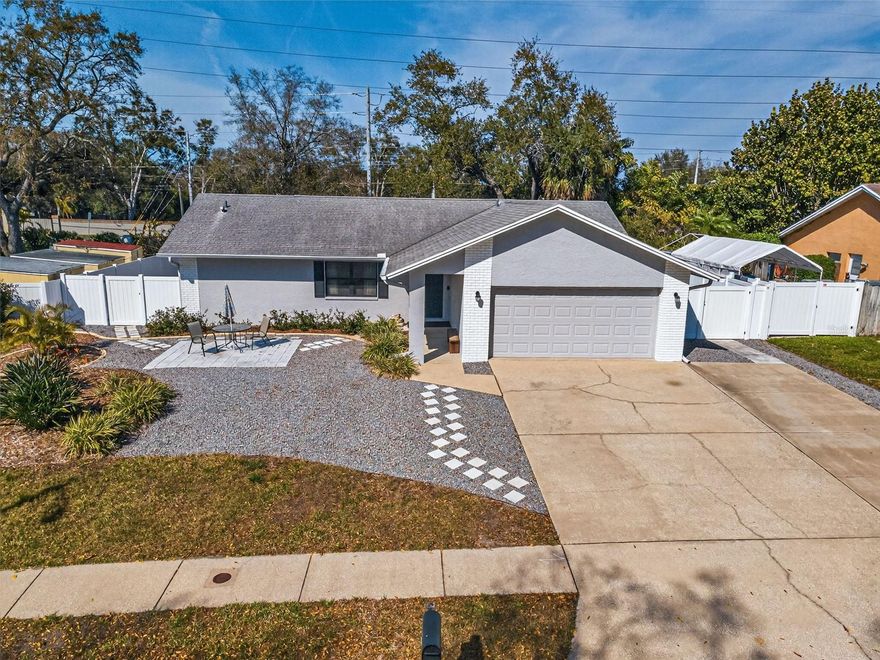 This picturesque Palm Harbor home boasts the sweeping curb appeal you’d expect to find in such a sought-after enclave. With 3 bedrooms, 2 full baths, and a 2-car garage, this ranch style/block construction home features a 3-car driveway that borders several tiled walkways: one leads to a spacious concrete patio, another to an inviting covered porch, and the third to a spectacular yard enclosed with a vinyl fence. A custom-built, screened lanai (with hurricane shutters) makes for a true retreat with ample room for dining, relaxing, and even space for your workout equipment. A serving port from the kitchen and a beautiful set of French doors from the formal dining room elevate the space to an entertainment destination for holidays and milestone celebrations. A huge stone patio extends well beyond the lanai’s footprint into the yard, reaching along both sides of the home lending tremendous design flexibility to this alfresco haven. There’s even the ideal construct to accommodate a cozy firepit. Inside, cathedral ceilings lend drama to the Great Room plan displaying a picture window and set of doors revealing the lanai. This expansive space allows an endless array of furniture configurations. The light and bright eat-in kitchen is well appointed with tons of storage space and a large pantry; the interior laundry room is fitted with newer appliances, plenty of cabinetry, and a utility sink. The split floor plan encompasses all three bedrooms which are carpeted and outfitted with generous closets, while the second bath was COMPLETELY RENOVATED with contemporary stylings. Only a quick drive to the famous Caladesi Island State Park, Honeymoon Island, eclectic Dunedin, Pinellas Trail, (the forty-seven-mile, multi-use pathway that runs from St. Petersburg to Tarpon Springs), and the unparalleled Clearwater Beach -- The Hammocks subdivision in Pinellas County is not in an evacuation zone and benefits from the stellar school district. An assumable VA loan with low interest is available for qualified buyers. This home on Foxcroft Drive has it all!