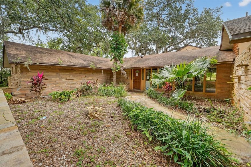 Where Architecture Meets Nature, A Rare Mid-Century Modern home. Tucked at the very end of a quiet cul-de-sac, is a private mid-century sanctuary situated on 1.62 acres of lush, natural landscape. A long private driveway leads you to this architecturally significant home, perfectly positioned to capture panoramic views of the pond and surrounding woodlands. Only a handful of properties have access to this peaceful non-motorized pond, offering a secluded setting ideal for canoeing, paddle boarding, wildlife watching, and quiet reflection.
The home itself is a striking example of mid-century design, featuring warm cedar tongue-and-groove vaulted ceilings, expansive glass to draw in natural light, and stunning splitface flagstone on the exterior and fireplace surrounds. The family room is a showstopper with its soaring ceilings, dramatic wood-burning fireplace, and views that stretch across the water. A second fireplace in the dining room creates an intimate atmosphere for gatherings, while the split floor plan provides privacy for the primary suite, which includes its own sunken hot tub outside. Guest bedrooms open to private decking, allowing each space to connect seamlessly with the outdoors. A screened atrium-style patio creates an indoor-outdoor flow perfect for entertaining or unwinding, while the three-car garage offers space for vehicles, storage, or a future workshop or studio.
The property is fenced and would be simple to gate for added exclusivity. The natural setting is unmatched, surrounded by mature trees and situated away from the road, this home offers the rare opportunity to live in peaceful seclusion while still being close to everything the Titusville area is known for. Residents enjoy access to local farmers markets, waterfront dining, boutique shopping in Historic Downtown Titusville, and front-row views of rocket launches from nearby Space View Park. Outdoor enthusiasts will appreciate being minutes from the Merritt Island Wildlife Refuge and Canaveral National Seashore with miles of unspoiled shoreline, trails, and kayaking access.
This is more than a home, it is a lifestyle. A property that speaks to the buyer seeking privacy, land, architectural character, and the opportunity to create long-term equity while preserving a timeless design aesthetic. Homes with this combination of acreage, water access, and mid-century appeal are exceedingly rare to find. This is your chance to own a legacy property and define its next chapter.
This is more than a home, it is a lifestyle. A property that speaks to the buyer seeking privacy, land, architectural character, and the opportunity to create long-term equity while preserving a timeless design aesthetic. This is your chance to own a legacy property and define its next chapter.