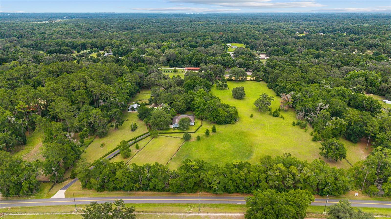 Discover this beautifully maintained 14.8-acre horse farm in the heart of Ocala’s desirable Northwest horse country—just minutes from the World Equestrian Center, HITS, and located within the coveted Horse Preservation Area. Tucked behind custom double iron gates with lush landscaping and a paved asphalt drive, this turnkey property blends timeless elegance, functionality, and privacy into one breathtaking equestrian estate. At the heart of the property is a warm and welcoming 3-bedroom, 2.5-bath home with 3,487 total square feet that effortlessly balances comfort and style. The home’s layout is designed for both everyday living and entertaining, featuring a formal dining area and a charming breakfast nook framed by a bay window that overlooks the grounds and screened-in pool. The open-concept kitchen and living area offer a seamless flow, highlighted by an inviting bar—perfect for morning coffee—as well as expansive counter space, abundant cabinetry, and newer stainless-steel appliances. The primary suite is a peaceful retreat, offering French doors that lead directly to the pool area, dual walk-in closets, and a spacious en-suite bathroom with dual vanities and a soaking garden tub. Two additional guest bedrooms are located on the opposite side of the home, providing privacy for family or visitors, and are served by a well-appointed full guest bath. Step outside to enjoy the farm’s true beauty—rolling pastures shaded by magnificent granddaddy oaks, five thoughtfully laid-out paddocks, and expansive open spaces ideal for a jump field or future cross-country course. Level ground also offers multiple locations suitable for building an arena. Equestrian infrastructure includes two barns with a total of ten 12x12 stalls, a large air-conditioned tack room, hay storage, a grooming stall, and three wash racks with insta-hot water, ensuring optimal comfort for both horse and rider. Equestrians will also appreciate the round pen, ample pasture space, and fully perimeter-fenced property, surrounded by a border of mature trees that provide additional seclusion and a tranquil, park-like setting. Recent updates include a new well pump, new A/C, and freshly painted fencing, showcasing the attention and care given to every corner of the farm. Adding further value is the charming tiny house, ideal for guests, caretakers, or seasonal rentals. This self-contained unit includes a full kitchen, full bathroom, laundry room, and a large living room window offering scenic views of the barns and pastures. There’s also an RV hookup, offering flexibility for visitors or traveling equestrians. This property has proven rental income, having been successfully leased during the winter circuit for both WEC and HITS competitors, making it not just a dream farm but a strong investment opportunity. Whether you’re an avid equestrian, a snowbird looking to be near premier horse venues, or someone simply seeking peace, beauty, and functionality in one of Florida’s most prestigious equine regions—this NW Ocala farm checks every box. Don’t miss the opportunity to own this one-of-a-kind farm in a location that offers both prestige and practicality. Schedule your private tour today and experience all this property has to offer.