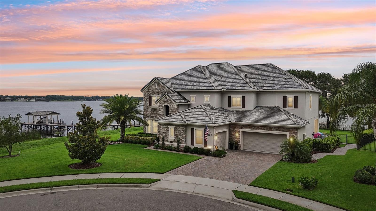 This one-of-a-kind, custom-designed lakefront estate sits at the very tip of a private island peninsula behind two exclusive gates, offering an unmatched lifestyle of privacy, tranquility, and luxury. With 350 linear feet of private lake frontage, you’ll enjoy both stunning sunrises and sunsets, plus unobstructed panoramic water views from nearly every angle.
Set on one of the most desirable and private lots available, this estate spans over 4,500 square feet of impeccably designed interior space with a long list of upgrades. The approach to the home features an expanded paver driveway and walkway, resort-style landscaping, and aluminum fencing. At the water's edge, a 130-foot Hodgskins dock awaits, complete with an 8,500-pound boat lift, water, and power—perfect for lake enthusiasts. The wraparound shoreline provides a natural, tranquil buffer and enhances the breathtaking scenery.
The outdoor living experience is truly exceptional. A stunning resort-style pool features elegant water elements, custom lighting, and professional curbing that elevates the landscaping while keeping maintenance low. The fully equipped summer kitchen includes Dekton countertops, a built-in grill, sink, ice maker, and ample prep space—ideal for hosting gatherings. Tongue-and-groove wood-paneled ceilings add architectural charm to the covered patio, while motorized retractable screens provides comfort throughout the year. Additional exterior features include custom landscape lighting, a full bug misting system, and a screened-in balcony with serene views of the lake.
Inside, you're welcomed by rich custom wood flooring, soaring ceilings with exposed beams, and expansive windows that flood the home with natural light and frame the lake views. The open-concept living area is anchored by elegant millwork and a seamless connection to the outdoors. The chef’s kitchen boasts premium appliances, upper cabinetry, two oversized islands, and a spacious walk-in pantry—designed for both beauty and function.
The first floor also includes a tranquil guest suite with a full bathroom, offering comfort and privacy. Upstairs, a theater/loft area features a dedicated wet bar with wine and beverage storage, perfect for entertaining. The custom laundry room impresses with abundant cabinetry, generous counter space, and an oversized farm sink.
The primary suite is a private retreat with a tray ceiling, two walk-in closets, garden tub, separate shower, dual vanities, and access to a private screened balcony with stunning lake views. All bedrooms are generously sized, and each bath showcases marble-tiled walls that bring spa-like elegance to daily routines.
Throughout the home, custom window shades provide privacy and light control. Smart-home ready, the property allows you to manage climate, access, and security with ease. The floor plan balances open gathering spaces and peaceful private areas, offering comfort and functionality for everyday living.
Located in the gated community of Hickory Hammock at Emerald Pointe, residents enjoy resort-style amenities including a clubhouse, pool, tennis and volleyball courts, fitness center, nature trail, community dock, playground, and dog park. Top-rated schools and conveniently located near shopping, dining, and major highways.
This is more than a home—it’s a rare legacy property offering unmatched privacy, peace, and connection to the water. Schedule your private tour and experience the pinnacle of lakefront living.