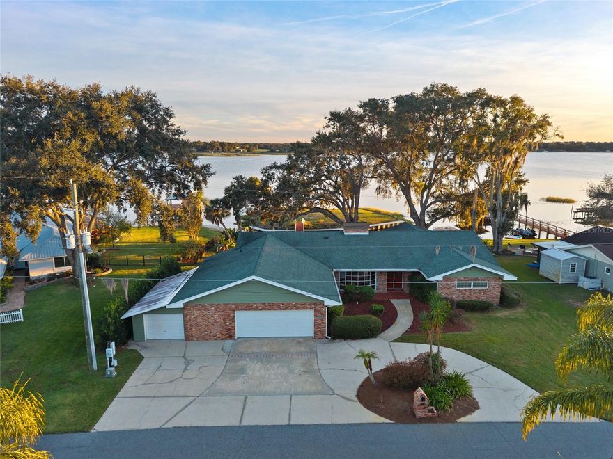 Experience the beauty of Lake Weir living at this stunning 3-bedroom, 3-bath lakefront home. Inside, you’ll find vaulted wood-beam ceilings, hardwood floors, and expansive windows framing breathtaking water views. The primary suite includes an office area and French doors that open directly to the lake, creating a peaceful retreat. The spacious kitchen offers granite countertops, stainless appliances, and plenty of room to gather. Step outside to an open brick patio surrounded by mature oak trees and take in spectacular sunsets over the water from your own private paradise—complete with a charming footbridge leading to your own island. An air-conditioned bonus room off the garage provides flexible space for hobbies or storage. Located in the desirable Bird Island neighborhood, just minutes from The Villages, this home offers the perfect balance of relaxation and recreation—with two waterfront restaurants on Lake Weir only a short boat ride away.