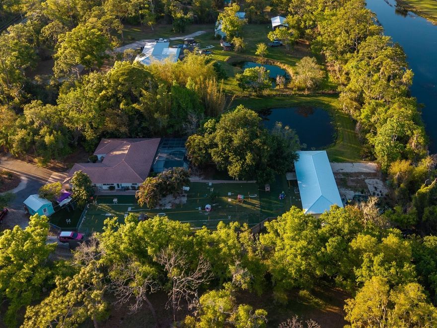 Gated Sarasota Estate with Home Business Infrastructure — Live, Work & Thrive on 2.49 Acres! Tucked deep off Proctor Road, this lakefront estate — w/ its own private pond — offers a rare convergence of privacy, space, & opportunity that simply does not come along often — at any price. Featuring a resort-style pool, spa, & elegant spillover feature—an inviting oasis set amid lush landscaping & tranquil lake views, designed for both relaxation & entertaining. The exceptional screened lanai & pool area transforms outdoor living into a private escape. The property is fully fenced, & a canopy of mature oaks & native Florida landscaping lines the paver arrival, where a courtyard entrance, stone exterior accents, tile roof, & French door entry set a tone that is warm, layered, & full of character. Inside, the open split floor plan spans 2,223 sq. ft. of air-conditioned living space, w/ upgraded windows throughout. Custom tile floors, wood tongue-groove ceilings, & handcrafted millwork weave a common thread of carefully articulated detail that connects each room’s distinct personality. The formal living room features a dramatic wood feature wall & sliding glass doors to the private courtyard; the dining room is anchored by a custom chandelier; & the family room opens to the screened lanai through sliding glass doors w/ recessed lighting throughout. The kitchen is the heart of the home — appointed w/ a center island, bar seating, black granite countertops, white raised-panel cabinetry, a built-in pantry, stainless steel appliances, two refrigerators, & a pass-through to the pool area, w/ more than enough room & storage to handle everything from a quiet morning to a full crowd. The primary suite is a true retreat — quiet, grounded, & thoughtfully appointed, w/ an en suite bath that feels spa-like, featuring dual sinks, an electric LED mirror, & a walk-in shower designed for unwinding, plus a pocket door leading to a built-in walk-in closet. Two additional bedrooms each feature the home’s signature tounge-groove ceilings & moldings, while the guest bath impresses w/ custom black-and-white tile floors & a subway-tiled shower-tub surround. The detached 77x24, fully air-conditioned 1,848 sq. ft. concrete block building — designed w/ concrete flooring & three garage bays w/ tall electric overhead doors, — is currently configured as a flexible, purposeful space. Think home business, car collection, woodworking shop, weekend projects, or whatever your passion demands — ideal for anyone who needs serious room to do what they do. The attached two-car garage adds 441 sq. ft. of enclosed, air-conditioned space. Both the house & concrete block building are insulated w/ Icynene spray foam & equipped w/ new AC systems & ductwork (replaced within the last 3–5 years), & the concrete block building received a brand-new metal roof in 2025. The sewer/drain line has also been re-lined within the last several years — the kind of behind-the-scenes investment that makes a real difference in long-term ownership. There is ample room for RV & boat parking, & w/ no HOA to contend w/, you have the freedom to use this property entirely on your terms. Located in a coveted enclave of just 12 estate-sized lots — minutes from Clark Rd & I-75, & a short drive from Siesta Key beach. Nearby trailheads provide easy access to the Legacy Trail, & the area is rich w/ shopping, dining, & parks.