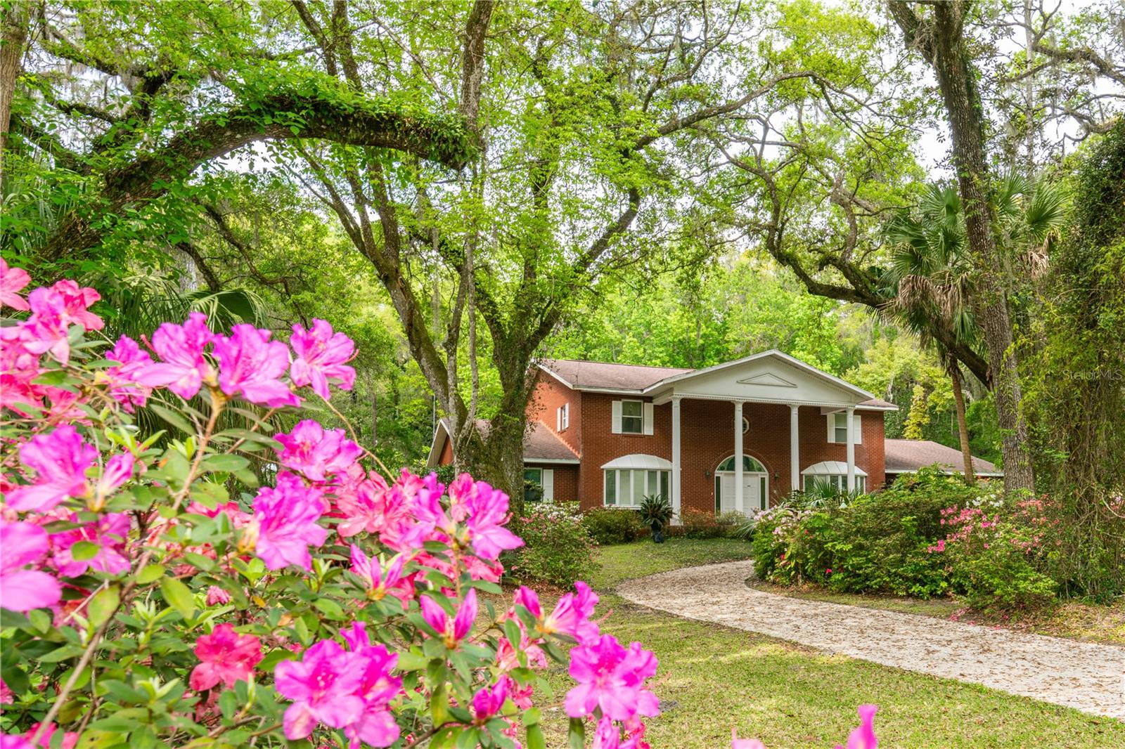 Step into timeless elegance with this custom-built British Colonial masterpiece, offering over 4,300 sq. ft. of air-conditioned living space plus an enclosed sunroom, spacious patio, and an oversized 2-car garage with additional storage. Set on 2.5 beautifully landscaped acres filled with fruit trees and flowering plants, this home offers space, privacy, and charm in equal measure. Built in 1983 by renowned builder Don Richards, the home features a solid brick exterior, a deep foundation, and unique architectural elements throughout. Inside, you'll find 5 bedrooms (including a spacious primary suite with private balcony), 4 full bathrooms, and thoughtful details that elevate every room—from 24-karat gold-plated fixtures to custom cut-glass accents framing the entryway. Enter through the tiled foyer with its soaring ceiling and arched doorways. The kitchen has been upgraded with granite counters and flows into a large laundry room and corridor. The living and dining rooms feature real polished wood floors, oversized bow windows, and elegant touches like a salon door and chandelier lighting. Relax in the sunken den, complete with rich wood paneling, a surround sound system, and a brick wood-burning fireplace. Adjacent, the bar/rec room boasts a tiled counter, wood paneling, and built-in benches with hidden storage. A cozy guest bedroom offers privacy in its own quiet corner of the home. Upstairs, the primary suite includes a carved wooden wardrobe, TV nook, and spacious bathroom with double sinks, dressing area, and balcony views over the backyard and neighboring farm. There are 3 additional generously-sized bedrooms, a study/library with built-ins, two smaller rooms perfect for hobbies or homework, and updated bathrooms with European bidets and dual sinks. Outside, enjoy your own private pool with a slide, electric heater, and an enclosed sunroom with lockable sliders and garden views. The home is equipped with 3-zone A/C, brand new water heater (2025), updated plumbing (2024-2025), and a durable roof in good condition. Additional features include: -Wired for alarm & intercom -Pool heater -Custom chandeliers (1 large, 7 small) -Attic storage -Colonial-style curved staircase -Iron security doors -Multi-use prayer room or pantry with built-in shelving. This property is an exceptional blend of character, comfort, and craftsmanship. Don't miss this rare opportunity to own a true Brooksville gem!