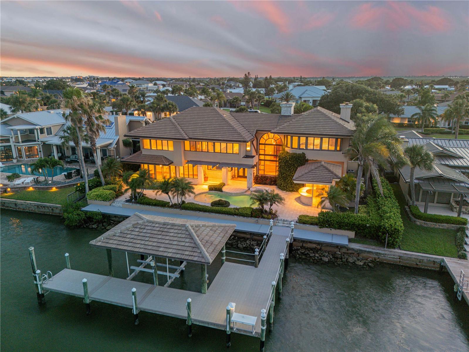 One of a kind direct Intracoastal Waterfront Oasis w 27ft Boat Lift, Resort Style pool, and located in one of the most esteemed communities in New Smynra Beach…Venezia. Quietly nestled at the end of Quay Assisi, this fully custom-built home offers an unmatched design combining a blend of sophistication, exquisite architecture, and breathtaking views from almost every position in the home. Enjoy distinctive touches such as a custom arched copper entrance leading to grand 10ft mahogany doors, unique mahogany trim work throughout, grand soaring ceilings adorned by keystone-clad columns, and beautiful stonework at every turn. Boasting 4 bedrooms, 4 full baths, and 2 half baths, this home is ideal for those seeking a private retreat tailored for both relaxation and entertaining. The expansive living room showcases a fireplace, massive vaulted ceilings, and captivating water views, while the formal dining room comfortably accommodates gatherings beneath exquisite alabaster fixtures that echo the home's overall luxurious and custom feel. The gourmet kitchen is equipped with top-tier amenities including a Sub-Zero fridge/freezer and induction cooktop, all framed by picturesque river panoramas. A ground-floor office with mahogany cabinetry provides a serene workspace, complemented by a secluded family room and separate guest quarters upstairs. Step through the rear doors out to a true river front oasis with a gorgeous pool overlooking panoramic views of the Intracoastal Waterway. The centerpiece of outdoor indulgence is a resort-style pool, seamlessly integrated with keystone surfaces, accompanied by a charming cabana-style covered outdoor kitchen ideal for alfresco dining and entertaining. With 100’ of frontage, the property boasts a substantial dock featuring new composite decking and a 27-foot boat lift, complete with 50-amp electric service. Here, every detail exudes elegance and functionality, offering an unparalleled retreat for those who cherish waterfront living at its finest. Local custom home builder, Will Miller, spared no expense with superior craftsmanship, including monolithic slabs, robust beams, and concrete block construction, ensuring both durability and comfort for the life of this home. Impeccably maintained by its original owner, the property radiates pride of ownership and retains a like-new appearance. Located on the beautiful isle of Venetia, this charming community features exquisite homes and offers an amazingly close proximity to the beach, Flagler Ave, Canal St, and all of the most popular restaurants and shopping NSB has to offer. You certainly will not find a more unique river front home with a dock, boat lift, and all the luxurious features this home has to offer anywhere else in the area. You simply must see this home in person to truly take in the feeling of grandeur and true elegance it has to offer. Call to schedule your home tour today! Be sure to check out the FULL VIDEO TOUR at https://youtu.be/d7EeSspkllE