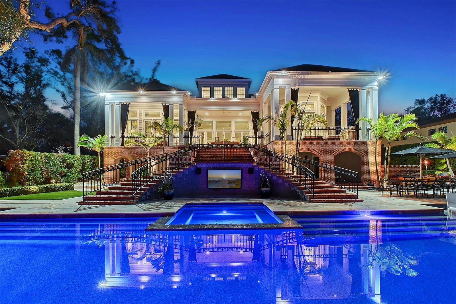 Nestled on the prestigious Bay Point Dr, this Georgian Colonial home blends timeless architecture & modern luxury. With over 6,300 sq.ft of high & dry living space—untouched by recent hurricanes—every detail of this four-bedroom, all-en-suite residence is designed for both grandeur & comfort. A stately front door opens to a grand foyer, flanked by a formal dining room perfect for entertaining & a classic living room ideal for quiet moments. The spacious great room offers an inviting area to relax or gather, seamlessly connected to an expansive chef’s kitchen outfitted with high-end appliances, generous counter space & an open layout that encourages connection. Recently updated bathrooms showcase luxurious finishes, refreshed tilework & elegant fixtures. A private theatre room provides an immersive escape for unforgettable movie nights. The oversized primary suite offers a spa-like bathroom & a massive walk-in closet, thoughtfully designed to accommodate the most extensive of wardrobes. Every detail reflects both comfort & sophistication. An impressive eight-car garage caters to collectors & hobbyists alike, offering ample room for vintage automobiles, motorcycles or storage. Outdoors, the property truly shines. Set along the picturesque Hudson Bayou, the backyard offers serene water views with the iconic Selby Gardens as a backdrop. Direct access to Sarasota Bay makes this a boater’s dream, with a private dock featuring a 27,000 lb lift (removable for a 70’ shallow-draft boat), 4’ depth at mean low water & approx. 6' in the channel—putting you in open water in under 2 minutes. The manicured lawn & terrace are enhanced by lush, refreshed landscaping, creating a vibrant, resort-like ambiance. Shaded seating areas, flowering foliage & sweeping green spaces make the outdoor areas ideal for both everyday enjoyment & elegant entertaining. This enchanting setting has hosted starlit weddings, milestone celebrations & joyful family gatherings, all with the natural beauty of the bayou as the perfect backdrop. Located between Harbor Acres & Downtown Sarasota, this home offers both privacy & convenience—just minutes to world-class dining, shopping, the arts & the bayfront. More than just a home, this is a rare opportunity to own a legacy property where luxury meets lifestyle & unforgettable memories are made. Welcome to Bay Point.