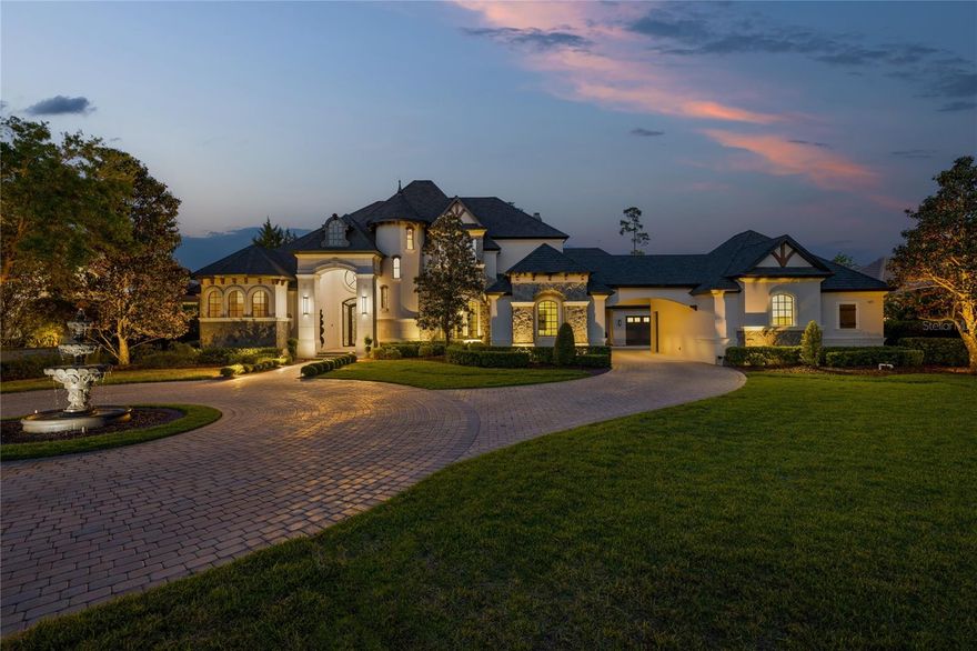 Experience the pinnacle of luxury living at this extraordinary estate, perfectly positioned on the 5th green of the prestigious Tom Fazio-designed Legacy Club at Alaqua Lakes. Privately nestled on 1.27 Acres within Alaqua, one of Central Florida’s most exclusive communities, this three-story custom masterpiece offers almost 8,000 square feet of artfully designed living space and over 11,000 square feet under roof. Originally built by a custom homebuilder for personal use, no detail was overlooked in the construction of this stunning residence. From the moment you step inside, you're greeted by soaring ceilings, exquisite custom millwork, rich wood accents, and refined finishes throughout. Formal living and dining areas transition seamlessly into the showstopping heart of the home, a spectacular open-concept kitchen and family room, with vaulted ceilings, stone fireplace, wet bar, the designer kitchen features top of the line appliances, a large center island with a prep sink, and a massive hidden walk-in pantry. The spacious primary bedroom suite features a gas fireplace, sliding doors leading directly to the covered lania and pool, and a spa bath with massive walk-in shower and a soaking tub. Additional highlights include a private elevator, bonus room with private staircase access, a study, and a home theater for the ultimate cinematic experience. Outside, your private resort awaits. The breathtaking backyard features a rock-formed tropical pool with waterfalls, a built-in waterslide, and a fire pit lounge designed to rival any luxury retreat. Entertain in style beneath tongue-and-groove wood ceilings at the summer kitchen, gather around the outdoor fireplace, or unwind in the open-air shower after a dip in the pool. The well-manicured grounds also include a 5-car garage with portico, fenced yard, circular drive, and a stately fountain that sets the tone for this magnificent residence. Alaqua is conveniently located near boutique shopping, dining, hospitals, and major highways, providing easy access to downtown Orlando, world-renowned attractions, pristine beaches. The community features a private 18-hole golf course designed by Gary Player featuring elevated tee boxes and beautiful, picturesque fairways. Don’t miss your opportunity to own this one of a kind residence.