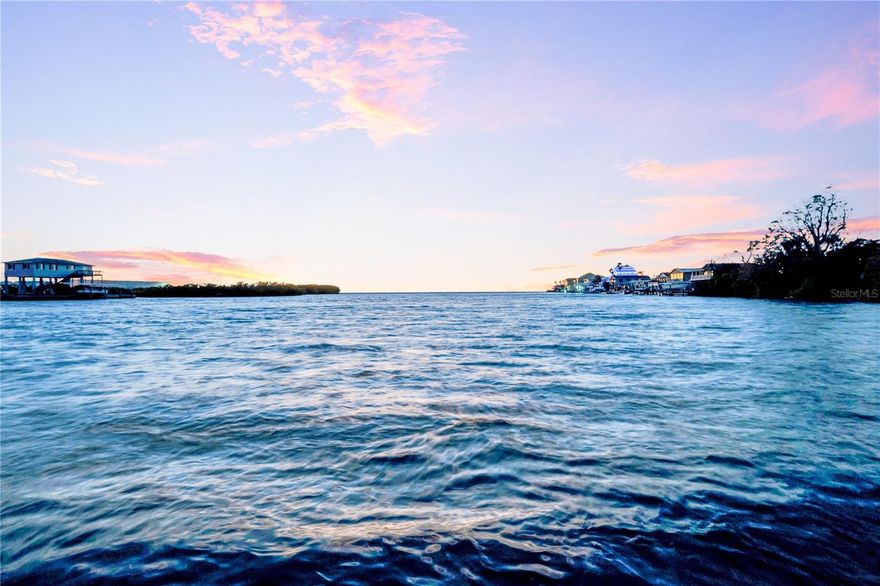 POETIC & PEACEFUL. Ideally positioned on a wide water basin with natural buffering and direct, unobstructed access to the Gulf of Mexico. This elevated waterfront home offers breathtaking sunset views and water visibility from all living areas. Custom built by the current owner, this home has been meticulously cared for and proudly maintained by its original owner since construction. The main living area features soaring vaulted ceilings ranging from approximately 10 to 16 feet, expansive windows at every angle, with a double sided wood burning fireplace connecting both the great room and the primary bedroom. The home offers 3-bedrooms and 2-bathrooms with approximately 1,800 square feet of heated living space. A private elevator services the home. A spiral staircase provides additional access from the garage to the main living area. Below the home is approximately 1,640 square feet of garage space, offering extensive storage and flexibility. Covered outdoor living areas include approximately 1,200 square feet of open porches, creating multiple spaces to enjoy coastal breezes and sunsets. Items worthy of mention; Full HVAC system replacement in 2024 with a hypoallergenic filtration system added, complete new roof installed in 2019, (4) garage doors replaced in 2024, 80-gallon solar water heater (2018), whole house fan system, hurricane shutters and panels throughout, The home is equipped with (2) whole home electrical shutoffs, main electrical panel and subpanel, and a Goldline whole home electrical surge protection system installed at the main panel. Stand up attic space with pull down ladder access, offering convenient storage and accessibility. The interior was fully painted in 2017 and the exterior was pressure washed in January 2026. Custom wood flooring selected by the owners, crafted from a blend of red and white oak harvested from an 80-acre wood lot in Michigan. Please note the four-car garage features approximately 20-foot ceiling height, and about 15-feet of clearance to the bottom of the rafters. Three garage doors are standard height at approximately 7 feet, with one oversized garage door measuring approximately 11 feet, ideal for larger vehicles or specialty storage. A well-maintained seawall with substantial concrete capping enhances the waterfront setting. Boat lift present and not currently operational. Charming waterfront cutout along the concrete seawall creates an intimate spot for launching kayaks, quiet fishing, or enjoying peaceful water view. Surrounded by mature trees and coastal habitat, the property regularly attracts dolphins and manatees and there is abundant birdlife including pelicans, herons, egrets, cormorants, loons, pileated rose beaks and other native species. Come own your Elevated Coastal Serenity today. Professional Video & Floorplan available upon request. Every day, your view unfolds like a living masterpiece, changing moment by moment.