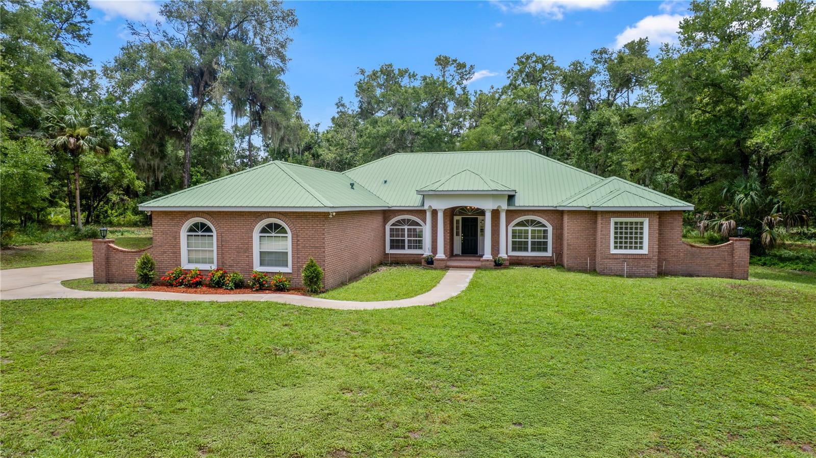One or more photo(s) has been virtually staged. Situated on a 2.77 acre lot and boasting with over 3,100 square feet of spacious living, this home is truly a rare find. Welcome home to this beautiful 4 bedroom, 3 bathroom custom-built home with a oversized two-car garage. The brick home offers a classic design while the metal roof offers peace of mind and an upgraded look. Step inside and by greeted by this thoughtfully designed split floorplan with lofty ceilings throughout the home. The gourmet kitchen is equipped with granite countertops, cherry wood cabinetry and tray ceilings throughout the kitchen and living space, offering a elegant touch. The kitchen and living space seamless flow together with the living room offering a custom-built in cherry wood entertainment center with open shelving and a gas fireplace. The primary suite offers a peaceful retreat with an ensuite bathroom featuring a garden tub and walk-in shower and dual sinks, oversized dual closets, and private french doors which lead out to the covered lanai. On the opposite side of the home, you will find another bedroom with an ensuite bathroom, offering flexibility for multigenerational living or for guests. Two additional bedrooms and a full bathroom can also be found throughout the home as well as a formal dining room and sitting room which could be serve as a home office. Step through the french doors onto your covered outdoor lanai, already equipped with gas, electric, and plumbing for the outdoor kitchen of your dreams. Surrounded by nature, this backyard offers a serene and tranquil atmosphere with plenty of space for a future outdoor pool and spa. Located in the highly sought after Glenwood area and in a gated community, this home offers convenience to restaurants and shops. Located on 30 minutes from beaches and in close proximity to I4 for commuting. This home is a rare gem! Schedule a private showing today and make this custom-built house your forever home!