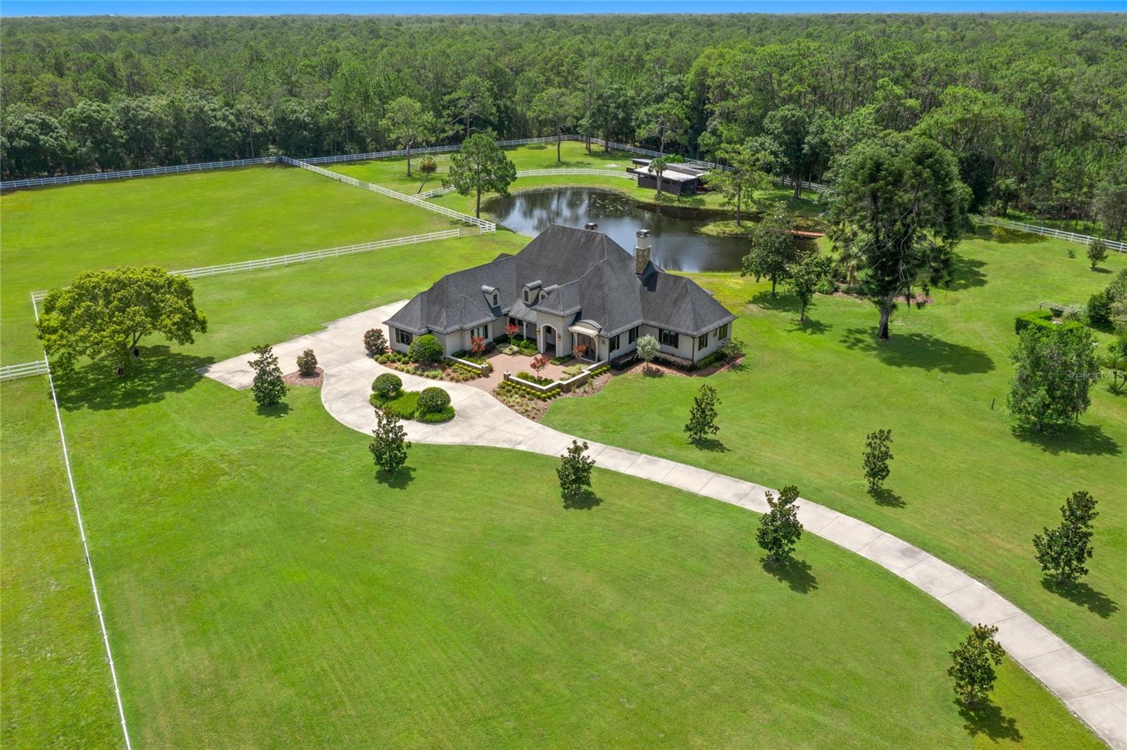 This luxurious custom built residence stands on nearly 13 acres of private fenced property surrounded by the largest natural preserve in Pinellas County spanning over 8700 acres of protected land creating ultimate privacy. Truly one of a kind! Welcomed through the grand entryway, you will notice soaring ceilings, a wide open layout, the impressive wood burning fireplace, exposed wood beams throughout the ceiling and wall to wall windows and doors flooding the interior with natural light with breathtaking views of the pond and endless lush greenery. The well designed kitchen is a chef's dream equipped with recessed cabinets and appliances, Wolf 6 Burner/Griddle combo, Pot Filler, Built in Miele Refrigerator and Freezer (side by side) with tailored cabinetry coverings, 2 dishwashers, warming drawer, speed-oven/microwave, ice maker, beverage cooler, an instant hot faucet, dual sinks, walk in pantry, and an oversized island open to the living room and dining space. The divine master suite presents marble flooring, a tray ceiling, and stunning views through the large windows and french doors to the backyard. Enter the opulent en suite with a soaking tub also with picturesque views, a large glass rainfall shower, dual vanities, dual sinks, and walk in closets. The large bonus living space includes wall to wall glass doors, perfect for an office, 2nd living room, den, library, etc. There is a powder bath for convenience located off the entry hall which follows toward the nice sized laundry room and 3 car garage entrance. There are 2 additional bedrooms and a bathroom located on the opposite side of the master suite for family or guests. The upstairs leads to an expanded loft, additional bedroom, full bathroom and bonus space. The outdoor patio includes an outdoor fireplace, and kitchenette with the most serene views. This home was carefully and quality crafted. 5 star energy rating/efficient, impact windows, no carpet (oversized ceramic, marble, and wood) throughout entire home. There is a 7 stall stable located on the property including a hay room, shavings room, and tack room. A storage shed is located out back for additional necessities. NEW ROOF 2023. The driveway includes a circular leading to ample parking, and a 3 car garage. Extreme Privacy abounds. Easy access to dining, shopping, entertainment and more. Only 15 minutes to beautiful Florida Beaches, Historic Downtown tarpon Springs, The Famous Tarpon Springs Sponge docks, 30 minutes to Tampa International Airport.