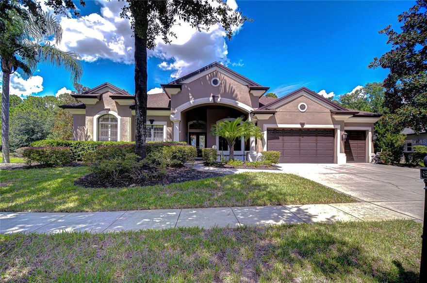 Stately executive residence on a picturesque wooded cul-de-sac with a tranquil side pond and back stream, this Arthur Rutenberg St. Augustine V model is perfectly situated in the exclusive, highly sought-after GATED waterfront community of Pasco Sunset Lakes.
From the moment you arrive, the portico-covered entrance framed by tall pillars and a welcoming front porch accented with half-pillars sets the tone. NEW Roof 2024! HVAC 2021! Glass double front doors invite you inside, where timeless architectural details and traditional charm blend seamlessly with an open-concept design. This expansive 1-story home boasts 3,609 sq ft, 4-Bedrms, 3.5 Baths, 3-Car garage. Soaring ceilings, crown molding, Plantation shutters, archways, columns, rounded corners, and desirable 3-way split-bedroom layout provide ultimate privacy for families and guests.
The gleaming ceramic tile floors flow throughout the main living areas, beginning with a dramatic foyer. Here, French double doors open to a large office with rich hardwood floors, while a stylish guest bath with pedestal sink and mantle sits just across. A pony wall with a decorative column separates the foyer from the formal dining room, enhanced by a tall, arched window that fills the space with natural light.
At the heart of the home, the chef’s kitchen impresses with 42-inch solid wood cabinetry topped with crown and display space above. A tile backsplash with decorative inlays complements the granite counters, while an extended hi-top breakfast bar and center island create plenty of space for cooking and gathering. Premium appliances include a Professional Wolf natural gas cooktop with vent hood, GE Monogram double ovens with convection and microwave, built-in refrigerator, and Bosch dishwasher. A separate dining area with bay windows overlooks the sparkling pool.
The living and family rooms, each adorned with sliding Plantation shutter panels, open wide with pocketing sliders to reveal the screened lanai, paver deck, and heated pool with a spill-over sheer descent waterfall—a private outdoor oasis that blurs the line between indoor and outdoor living. The family room features a tray ceiling, while the living room showcases a striking coffered ceiling, fireplace with mantle, and custom built-ins with glass shelving. This thoughtful design creates the perfect balance of elegance and warmth for everyday living and entertaining.
The opulent primary bedroom retreat with rich designer carpet and stunning tray ceiling has a sitting area with bay windows crown molding and French door access to the pool. Two separate walk-in closets contain pull-outs, shelves, drawers, bins, and more. The luxurious ensuite bath features a tray ceiling, crown molding, dual granite topped vanities, make-up area, deep soaking Jacuzzi tub with spa jets framed by columns and an arched window, a walk-in tiled shower with Listello accent, and private water closet.
Two additional bedrooms share a Jack and Jill bath, while the 4th bedroom/bonus/flex space features convenient access to a full pool bath and French door leading to the picturesque backyard—an inviting setting where you can relax with peaceful views and the chance to spot local wildlife.
Residents enjoy exclusive access to a private beach club, boat ramp, 42-acre ski-lake, playground, and more. Minutes from major highways, shopping, dining, and top-rated schools. Don’t miss this rare opportunity—schedule your private showing today and make this dream home yours!