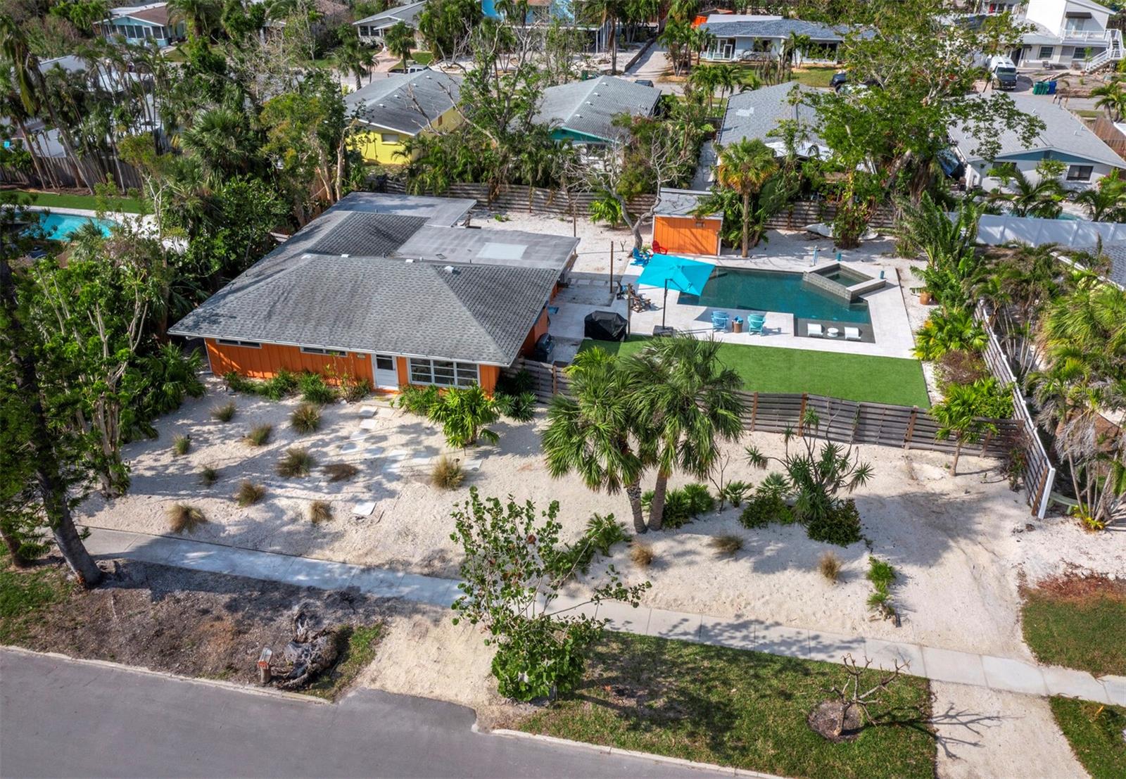 This standout property is back on the market due to a change in buyer circumstances and is ready for its next visionary owner. It's an ideal opportunity to renovate or build your dream home. In the heart of historic Longbeach Village on Longboat Key's north end, this charming mid-century cedar-framed residence is set back on an expansive elevated lot with a deep front yard. The property boasts a private oasis in the rear, complete with a generous pool, spa and low-maintenance lawn. Previously updated to blend modern convenience with vintage character, the home was featured in a 2022 Herald-Tribune article as A Sweet Spot on Longboat. Original details include terrazzo floors with flecks resembling sea glass and distinctive jalousie and awning windows, preserving its unique charm. The open concept living room and kitchen areas showcase cathedral-height ceilings, enhancing the sense of space. Modern drop lighting accents the kitchen and the layout offers easy flow and a relaxed living experience. A vibrant orange exterior and the light-filled rooms contribute to the home’s bright, uplifting atmosphere. Additional spaces include a generous den, a bonus room and an office, offering versatility for various needs such as a fourth bedroom if desired. The outdoor deck is ideal for entertaining or relaxing, surrounded by lush tropical landscaping. Following storm damage during the 2024 hurricane season, this property presents a unique opportunity to reimagine its full potential. Interior photos include images from before and after remediation. All exterior photos of the yard, pool, and spa are current. Enjoy Gulf-to-Bay access, perfect for beachcombing, boating, kayaking, and paddleboarding. The neighborhood offers proximity to waterfront dining, shops, and the ultimate Florida lifestyle. Longbeach Village features a boat ramp, bay access, public beach entry, and several restaurants, cafes, and fitness studios all just a few blocks away.