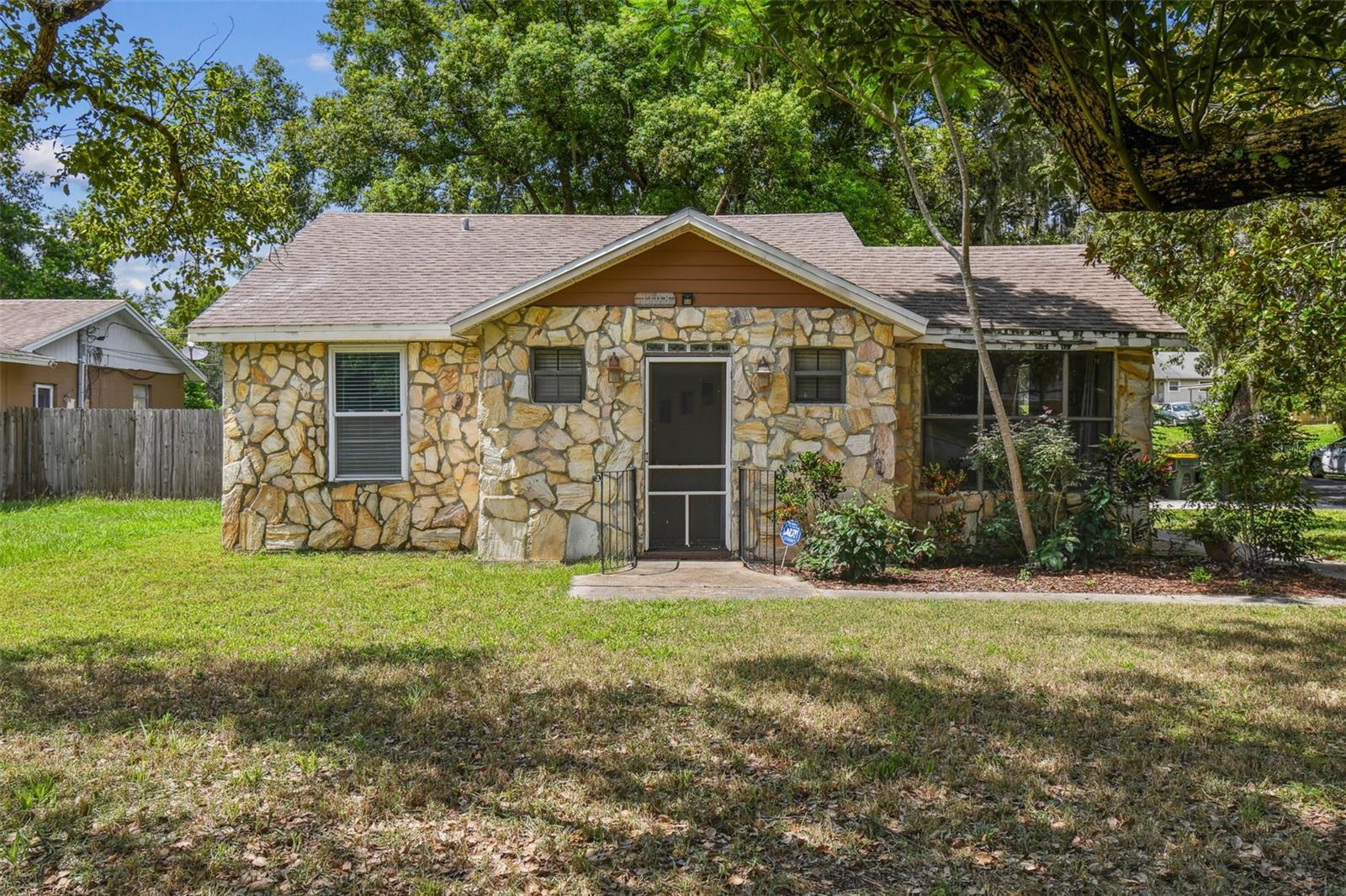 Charming Stone Cottage with Rustic Warmth & Modern Touches on a CORNER LOT! Discover this unique and inviting home, featuring a distinctive stone exterior and surrounded by mature trees, right in the heart of Clermont, offering a sense of privacy and natural beauty. Step inside to find a blend of rustic charm and functional updates, perfect for comfortable living. The interior boasts beautiful wood paneling and exposed beam ceilings in the living areas, creating a cozy and welcoming atmosphere. The spacious living room is ideal for relaxation, while the adjacent dining area, illuminated by a classic chandelier, provides a perfect setting for meals. Enjoy abundant natural light streaming through the large windows in the dining space. The kitchen, visible from the living area, features modern stainless steel appliances, ample cabinetry, and a practical layout for everyday cooking. The thoughtful floor plan flows seamlessly, offering a comfortable living experience. Outside, the property presents lovely curb appeal with its stone façade and mature landscaping, including large trees providing shade and character. This home offers a wonderful opportunity to embrace a unique aesthetic with a warm, inviting feel. All the major systems have been taken care for you providing you peace of mind for years to come - NEW ROOF being installed prior to closing, new water heater has been installed, and the HVAC system was replaced in 2021. Best of all, this home is located in the heart of Clermont - minutes from downtown Clermont and all the shopping, dining, and entertainment along Hwy 50. Lake County Schools is also rated A+ with great options nearby! Come visit this fantastic opportunity.