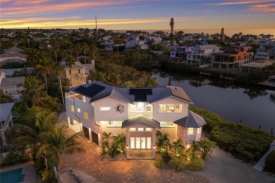 This waterfront coastal retreat embodies refined island luxury, offered completely turnkey and thoughtfully designed for both elevated living and exceptional entertaining. Positioned on a quiet cul-de-sac the home makes an immediate impression with its stately architecture, paver driveway, lush tropical landscaping, and landscape lighting that beautifully illuminates the property at dusk. Inside, travertine flooring flows throughout, complemented by crown molding in every room and tray ceilings that add architectural depth and sophistication across all three levels. The top floor serves as the heart of the home, where an expansive living and dining area is framed by large sliders that capture vibrant sunset skies and lead to two generous balconies, seamlessly blending indoor and outdoor living. The chef’s kitchen is a showpiece, appointed with premium Monogram appliances, a professional gas range with pot filler, custom cabinetry, striking backsplash detail, and abundant counter space designed for effortless entertaining. The living room offers an abundance of natural light that frames a beautiful fireplace adding an elevated ambiance. Designer lighting, custom stair railings, and carefully curated finishes create a cohesive coastal elegance that feels both polished and welcoming. The mid-level hosts 4 spacious bedrooms enhanced with shiplap accent walls in select rooms, adding warmth and texture, along with a comfortable family room that opens to an oversized balcony overlooking the tranquil bayou. A private elevator provides convenient access to every floor, while modern enhancements including a security system, Sonos sound system inside and out, solar panels, and a tankless hot water heater deliver efficiency and peace of mind. Outdoors, the property transforms into a true waterfront oasis featuring a sparkling heated pool and spa, fire features, expansive paver deck, screened-in patio lounge area, and multiple covered spaces ideal for year round enjoyment. The private dock is equipped with electric and water, offering boating access and completing the ultimate Florida lifestyle experience. The pass-through two car garage, paired with separate storage rooms is designed to accommodate lifestyle amenities and the home’s location within a short-term rental zone presents outstanding investment potential. From sunrise coffee on the balcony to sunset reflections dancing across the bayou, every detail of this exceptional residence has been thoughtfully designed to capture the very best of coastal living.