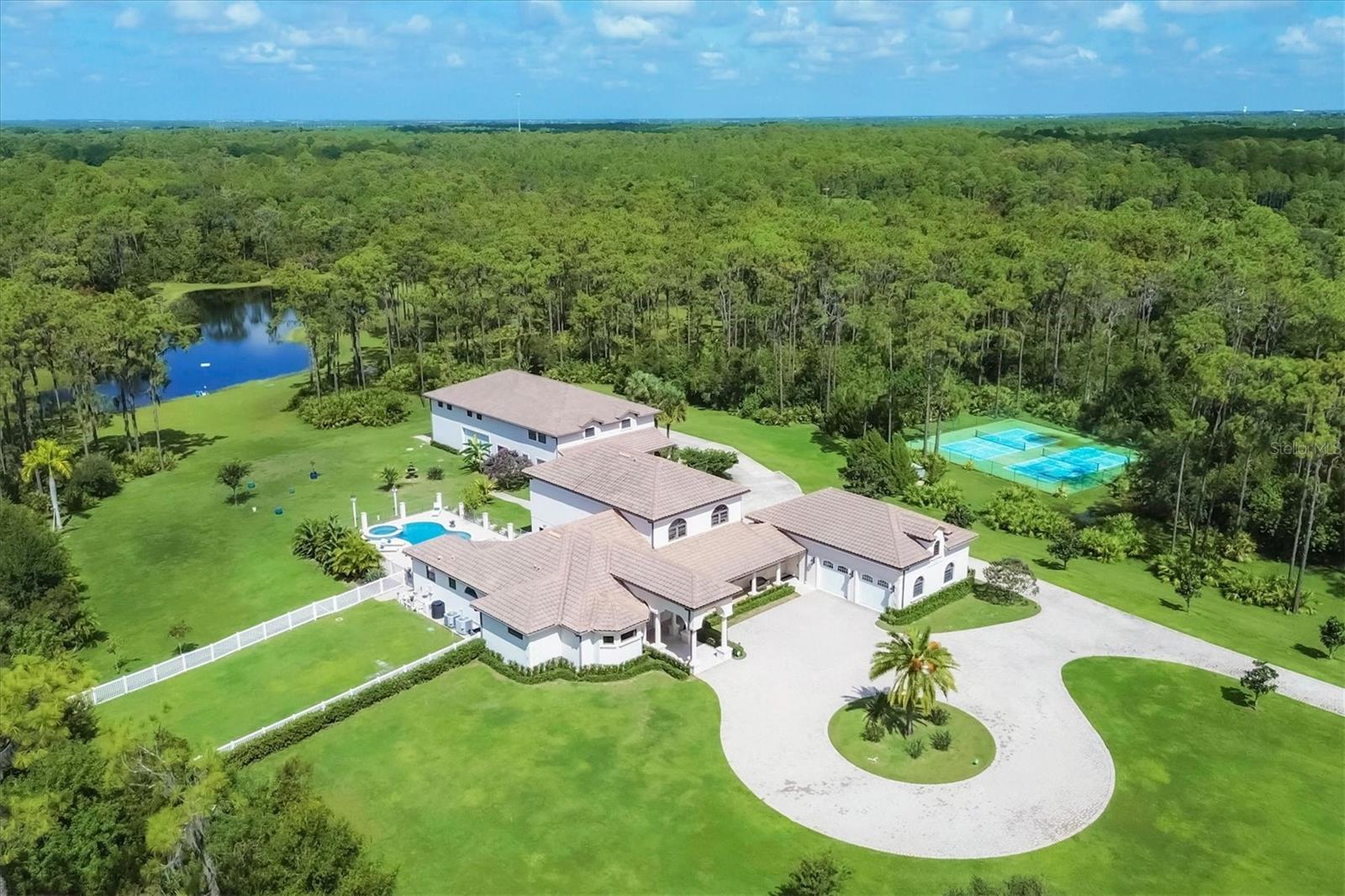 Location, Location, Location! HURRICANE SAFE PROPERTY and NO flood Zone !
Nestled in the equestrian community of Foxwood at Panther Ridge in Bradenton, FL, this extraordinary 13-acre estate redefines luxury country living while providing unbeatable location advantages. Just minutes from the vibrant Lakewood Ranch, top-rated schools, and the sandy beaches of Sarasota and Bradenton, this property is perfectly positioned for those seeking both tranquility and convenience.
This gorgeous, hurricane-safe property features two distinct homes, catering to those who value both comfort and adventure. Arrive via a scenic driveway to a grand entrance, where a stately columned front porch sets an elegant tone. Inside, arched doorways and regal columns enhance the home's grandeur. The main residence, a five-bedroom masterpiece, greets you with solid double doors that open to immediate views of the sparkling pool beyond the living room. A gas fireplace anchors this inviting space, making it perfect for entertaining.
For the culinary enthusiast, the gourmet kitchen offers sleek Patagonia Brazilian granite countertops, high-end Miele appliances, a large island, a breakfast bar, and an oversized walk-in pantry. Italian-sourced European light fixtures add an artistic and intricate touch. Centrally located, the kitchen and family room are designed for effortless entertaining.
The luxurious master suite features a second fireplace and direct access to the outdoor deck, enhancing the seamless indoor-outdoor living experience. The master bath offers a soaking tub, a Roman shower, dual vanities, and custom leather-wrapped closets for an ultra-luxurious feel.
The outdoor living area boasts a heated saltwater pool and spa, a covered deck, and a fully-equipped kitchen with a grill, range hood, and wine refrigerator. A wood-paneled ceiling adds a touch of country charm. The meticulously landscaped grounds include a fenced dog run, double tennis courts, and a private fishing pond, all illuminated by 300 landscape lights.
Practical upgrades include a new 600 KW Gillette commercial generator, a Culligan water softener, a 1,000-gallon propane tank, and a gas pump system with 93-octane fuel for your recreational vehicles. Upgraded LED lighting and built-out garage cabinetry present modern conveniences.
A separate guest house features three bedrooms, a living area, a laundry room, and a bonus room, perfect for guests or extended family. The main house offers a four-car garage, while the guest house includes a six-car garage with a workshop.
Equestrians can take advantage of the option to add horse stalls and jumping rings on the property. Enjoy 15 miles of trails for horseback riding and hiking in Panther Ridge, offering endless outdoor adventures. Plus, you're just moments away from Lakewood Ranch’s shopping and dining, top-rated schools, and the beautiful Gulf beaches.
This property is more than a home—it’s a lifestyle, offering luxury, safety, and a premier location.
Tax records show 6,541 sq ft of living space and 10,849 sq ft total, while MLS data indicates 6,774 sq ft of living space and 10,946 sq ft total. The main house includes five bedrooms, three full baths, two half baths, and a four-car garage. The guest house features three bedrooms, two baths, and a six-car garage.
All information is from the seller’s MLS listing.