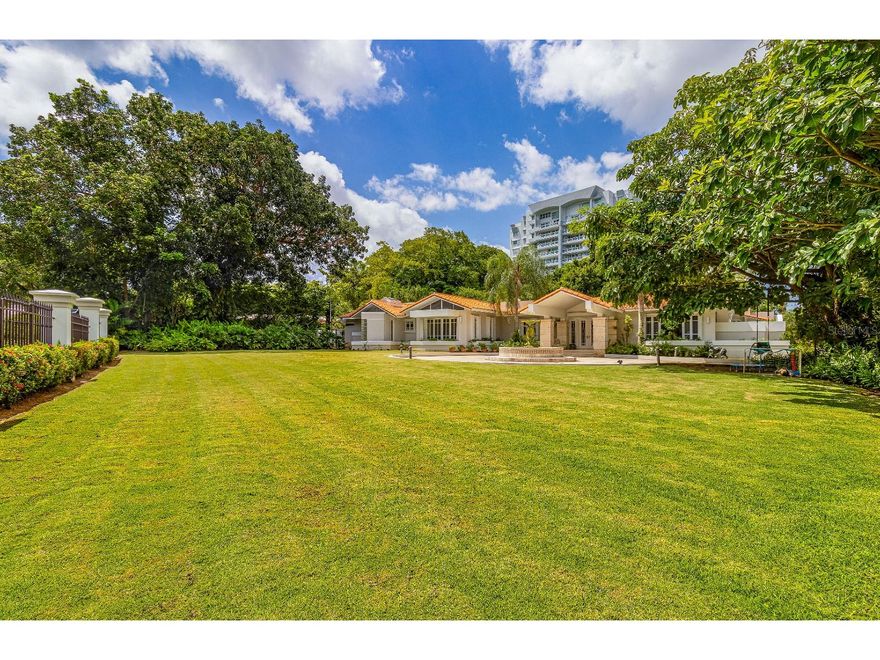 Nestled within the exclusive enclave of San Patricio, Guaynabo's most sought-after residential address, this exceptional one-level home offers an unrivaled blend of elegance, space, and timeless architectural design. Crafted in 1994 by the esteemed architectural firm Manuel J. Garcia & Associates, this residence showcases a timeless, classic architectural style and the comfort of one-floor living. With a generous 5,887 square feet of interior living space, complemented by an additional 1,575 square feet of outdoor areas, this home boasts a grand total of 7,462 square feet of luxurious living.
A charming front porch and welcoming foyer lead to a home office, an elegant living room, and a formal dining room offering serene views of the front yard. The fully equipped kitchen, designed with classic aesthetics, features both indoor and outdoor breakfast areas, perfect for relaxed gatherings. The main bedroom wing encompasses three generously proportioned bedrooms, easily convertible to four, ensuring ample space for family and guests. Each bedroom is an ensuite retreat, and there are a total of 7.5 bathrooms. The primary suite boasts a lavish master bathroom and separate dual closets. Adjoining bedrooms open up to a second family room making it an ideal place for studying or play area.
Situated on a spacious 4,756.37 square meters lot, the residence offers both front and back yards. The front yard is perfect for hosting events, while the back yard, with its terrace, gazebo, and inviting pool, is an entertainer's dream amidst lush and mature vegetation. Architectural plans are readily available to facilitate a second-floor expansion for additional bedrooms or features. The expansive lot also provides opportunities for additional buildings, such as lounges, garages, or additional terraces.
San Patricio is an exclusive gated community, comprising only 53 properties, each on a 1-acre+ lot. Enjoy 24/7 security and a central location providing easy access to major roads, schools, and entertainment. This home is fully equipped, completely air conditioned, and has both a full-power backup generator and a water cistern for your convenience and peace of mind.
Priced below Appraisal Value. Don't miss the opportunity to tour this grand estate that offers the epitome of luxury living in the heart of Guaynabo's finest neighborhood. Contact us today to schedule your private viewing.