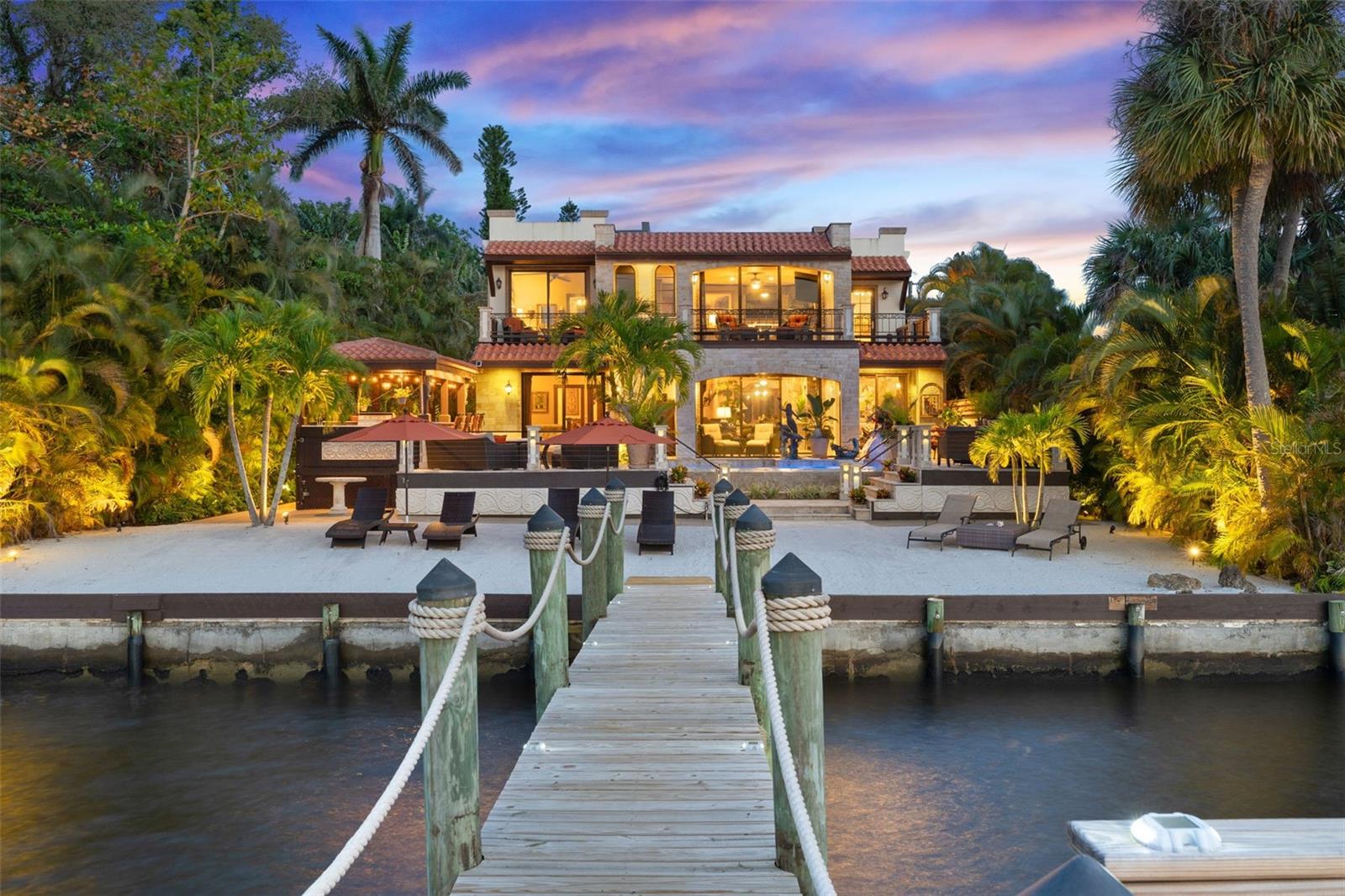 Welcome to your own private Mediterranean sanctuary on the Caloosahatchee River—where timeless design meets waterfront luxury in this fully custom-built, gulf-access estate. This extraordinary Spanish-style retreat captures the essence of paradise, offering sunsets over your private white sandy beach, a brand-new 200-foot dock with a 13,000 lb. boat lift. Step through the grand entrance into an expansive open-concept living space anchored by an imported stone fireplace. Walls of glass invite the outdoors in, drawing your eye to panoramic river views and the seamless transition to an outdoor oasis like no other. The centerpiece of this alfresco haven is a heated infinity-edge pool overlooking the river, a waterfall, and spa. The heart of the home is a chef’s kitchen tailored for culinary excellence, featuring bespoke cabinetry and plenty of space to gather and create. Each bedroom serves as a peaceful retreat, complete with its own en suite bath and private deck, where breathtaking river views greet you each morning. The primary suite is a masterpiece in itself—boasting direct access to the second-story wraparound porch, a luxurious bath with a triple vanity, walk-in California closet, and a spa-inspired shower experience. Ideal for hosting, the separate outdoor cabana is outfitted with a large grill, full bar, refrigerator, and sink. Meanwhile, the fully updated three-car garage—complete with air conditioning and a dedicated workspace—along with the expansive driveway, offers ideal storage for boats, creative projects, and ample space for RV parking. Above the garage, a completely remodeled one-bedroom, one-bath apartment with a full kitchen and patio offers the perfect guest quarters. This lushly landscaped and hardscaped property is elevated above flood grade and fortified with hurricane impact windows and doors throughout. With no neighboring homes in sight, the estate offers rare seclusion without sacrificing convenience or coastal accessibility.