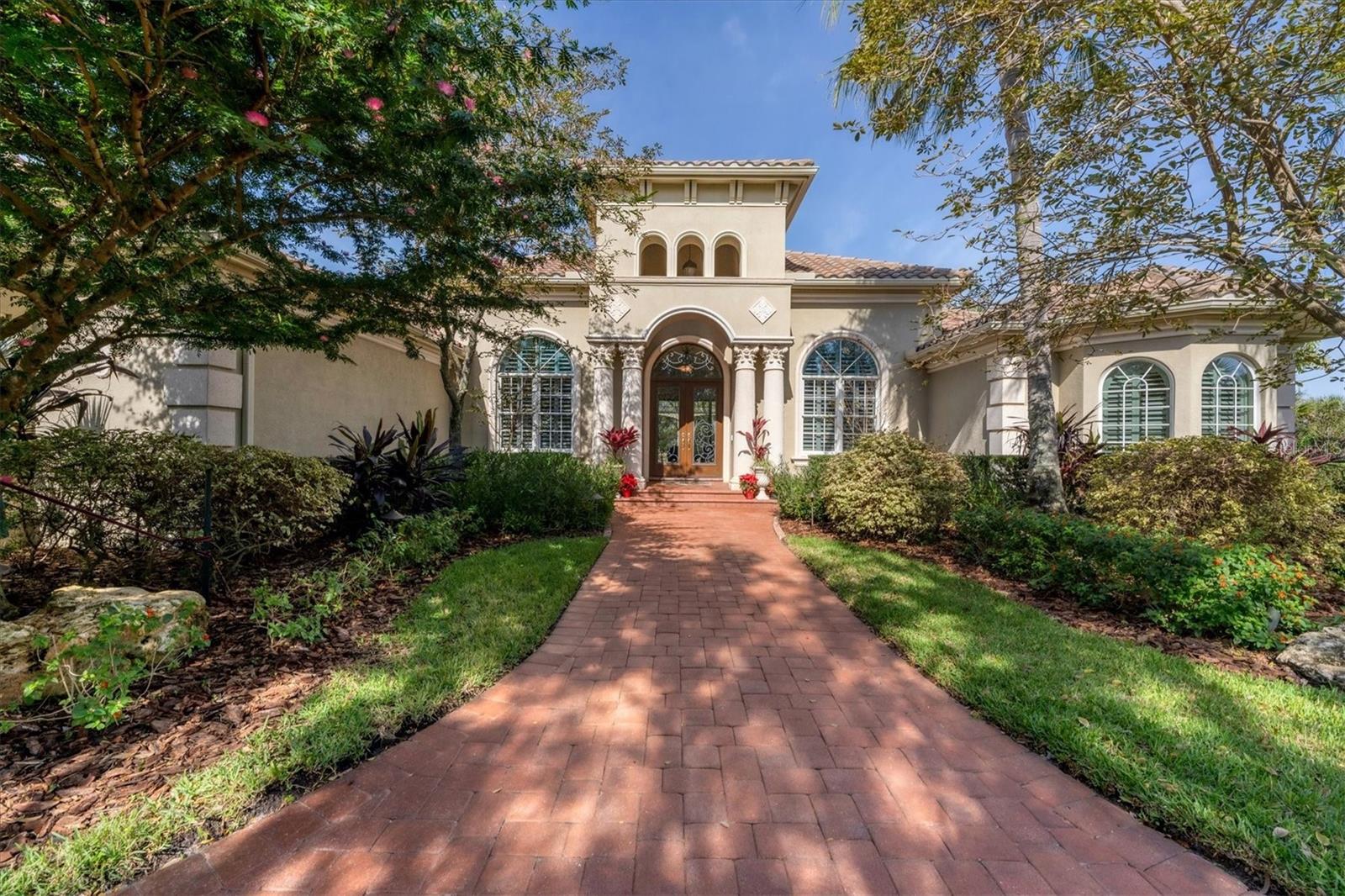 This impressive Pruett Mira Lago III estate home boasts a grand total of over 5,000 square feet of living space. It is perfectly positioned on a three-quarters-acre lot, featuring an extra-wide frontage and an expansive circular driveway. This magnificent residence was meticulously designed and constructed to embrace panoramic views of three distinct fairways: the 1st, 2nd, and 5th holes of the Robert Trent Jr. golf course, all while offering captivating lake vistas. It excels as an ideal residence for both indoor and outdoor entertainment.
The interior comprises three bedrooms, a library/office adorned with wood floors, and a custom-made "Gothic" style library bookcase equipped with up and down lighting, along with custom shutters. The chef's dream kitchen comes complete with an extra-large pantry. The living room, looks out into the lanai and boasts stunning views of the pool with its water features, lake and golf course. It features a gas fireplace and seamlessly connects to a formal dining room and a butler's wet bar, catering to your entertainment needs. There's also a room suitable for a piano or a second office. The primary suite offers a generously sized bedroom with an additional area for reading or relaxation. Two spacious walk-in closets with built-in shelves and drawers connect to an opulent bathroom with two water closets, a walk-in shower, whirlpool tub, and double vanity. One of the closets even features a built-in wall safe. The family room also boasts stunning views of the spectacular pool, lake, and golf course.
Adding to the luxury, an elevator takes you to a sizable upper floor. The second floor of this luxurious home is a haven for entertainment enthusiasts, featuring a spacious and elegantly designed area dedicated to leisure and enjoyment. The centerpiece of this level is a generously sized entertainment space that offers ample room for hosting gatherings, relaxation, and various recreational activities. The crowning jewel of this space is a beautifully appointed balcony that provides breathtaking vistas of the surrounding landscape. With sweeping views that extend beyond the horizon, the balcony becomes a tranquil retreat where one can bask in the beauty of the natural surroundings, making it an ideal setting for both indoor and outdoor leisure.
Inside, the residence is adorned with soaring ceilings and crown molding, an abundance of natural light, custom shutters throughout, stone columns, and a harmonious blend of tiled and wood floors, all tastefully complemented by a neutral color palette. The outdoor living space is truly impressive, featuring a well-appointed kitchen and a generously sized caged pool and spa. Clearview lanai screens, arches and up lit columns. Mature landscaping with extensive up-lighting. Spanish barrel tile roof and hurricane resistant windows and sliders throughout. Nestled within The Founders Club, a prestigious golf and country club community spanning 700 acres with 262 home sites, this luxurious property not only offers an exceptional home but also grants access to a plethora of community amenities. Conveniently located in Sarasota, Florida, it provides effortless access to I-75, downtown Sarasota, Gulf Coast beaches, shopping, and a diverse array of dining options, all just minutes away.