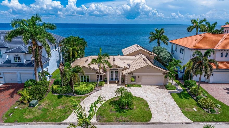 This exquisite waterfront residence in the highly desirable Venetian Isles neighborhood boasts an enchanting infinity-edge pool and unobstructed, captivating views of Tampa Bay. Recently updated, this 4-bedroom home showcases numerous quality upgrades, providing the essential Florida lifestyle experience. The entrance is graced by an oversized paved circular driveway leading to a beautifully etched French glass entry door. Upon crossing the threshold, you'll be immediately captivated by the ingenious floor plan, offering mesmerizing water vistas from the Foyer. The expansive living room with high ceilings and beams is perfect for entertaining and family life. It features a multi-slide wide door that seamlessly connects indoor and outdoor spaces, enhancing your overall living area and making entertaining a breeze. The contemporary oversized kitchen with gray-colored cabinets and striking exotic countertops exuding a distinctive character. Bosch appliances, including a five-burner gas cooktop, double oven, dishwasher, wet icemaker, and paneled Sub Zero refrigerator, cater to your culinary desires. The generous breakfast bar flows seamlessly into the luminous dining room, with high ceilings and a wall of sliding doors offering panoramic pool and water views. The stunning white weathered staircase ascending to the loft, currently utilized as a workout room and adorned with ceiling skylights, makes a great focal point. The floor plan of this residence is intelligently split to maximize comfort and privacy, with the waterfront master suite situated on the left side of the main living level. The primary suite features a reclaimed wood accent wall, convenient access to the pool patio, a spacious master bath, and a generous walk-in closet. A guest bedroom suite is conveniently positioned off the side by the main entrance. Two additional guest bedrooms are located off the kitchen and dining area, accessible through the hallway, while sharing a bright, beautifully updated bathroom. Elegant wood grain tile throughout the whole property makes for ideal flooring. The Travertine-tiled outdoor resort-style patio featuring a covered area with Pecky cypress ceiling and LED lights is designed to provide privacy and ample room for entertainment. Sliding doors span the length of the waterside, ensuring a seamless transition between indoor and outdoor living. The 25K gallon Infinity edge pool features a Jacuzzi, a spa waterfall, and a firepit overlooking Tampa Bay. Whether you're watching the morning sunrise or admiring the sunset sky from the pool, the patio boasts a convenient pass-through window and a bar ready to serve drinks and food. Adjacent to the pool deck is an outdoor kitchen with a Primo XL grilling station and ample bar seating to relax while observing pods of dolphins swimming by! A removable safety fence easily secures the pool deck. A lower-level Bayside deck leads to the permanent pilings, waiting for you to customize it to your needs. 90’ of updated seawall on this deep-water property, offering quick access with no bridges. Solar panels provide a substantial energy source for the entire property, including the pool equipment. Spacious two-car garage, complete with a workshop area has ample storage throughout. This slice of paradise seamlessly combines elegance and functionality. Located minutes from vibrant downtown St. Petersburg and 15 minutes to TPA.