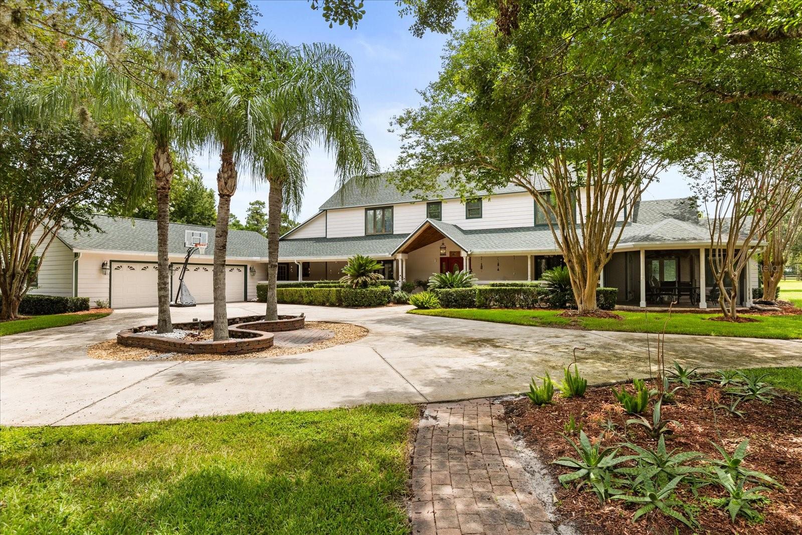 **This property qualifies for a closing cost credit up to $12,000 through the Seller’s preferred lender (restrictions apply).** Welcome to a Private Estate on Over 10 Acres in the Heart of Oviedo. Tucked behind majestic metal swing gates and down a paved drive, this 4-bedroom, 4.5-bathroom custom estate offers over 10 acres of serene, private living just minutes from city amenities. Featuring a 3-car garage, resurfaced saltwater pool, dual primary suites, and equestrian-ready facilities, this home balances refined comfort with functionality. A horseshoe driveway brings you to a charming paver patio with a built-in firepit—ideal for gathering. The covered, vaulted entry, with a bold red front door and sidelights, opens to a foyer showcasing a stone-lined fireplace and soaring ceilings. To one side lies a quiet sitting room; to the other, a formal dining room. The great room impresses with a wall-to-wall built-in bookcase and ladder, tall windows, and French doors that invite natural light and views of the property. The kitchen features rich wood cabinetry, stone countertops, a center island with cooktop, dual ovens, and a breakfast nook framed by a bay window. The adjacent laundry room adds convenience with upper/lower cabinetry, counter space, and a utility sink. This home boasts extensive updates: a new roof (2024), new HVAC (2024) with a second unit approx. 6 years old, and two water heaters (2024 and 10 years old). The saltwater pool was resurfaced in 2024, and the pool equipment replaced in 2023. A septic field was redone 3 years ago, and the home includes a reverse osmosis well water system and a 5-year-old water softener. For added functionality and peace of mind, the home includes a 500-gallon gas tank powering a whole-home generator. Additionally, a dedicated 220-volt power supply supports a kiln—perfect for ceramic artists or hobbyists. The main-level guest suite offers French doors to a patio with an above-ground spa and an ensuite with a glass-enclosed tub/shower. Upstairs, two more bedrooms include ensuite baths with glass enclosures; one opens to a spacious balcony overlooking the backyard and pool. The screened patio offers ample space for dining and lounging, with ceiling fans and direct access to an outdoor grill and the sparkling saltwater pool and integrated spa. Off to the side you will find a gazebo where the above ground spa sits and just steps away a space for nurturing young trees and plants. Outbuildings include two utility sheds, a greenhouse, stables, and a carport large enough for two golf carts—making this estate as practical as it is luxurious. The grand primary suite, tucked off the great room, offers vaulted ceilings, French doors to a private sunroom/office, and access to the front screened patio. Its luxurious ensuite bathroom features dual sinks, a walk-in shower that doubles as a steam room, and a freestanding copper Bateau-style soaking tub—the ultimate in relaxation. This one-of-a-kind Oviedo estate is move-in ready, combining timeless elegance, modern upgrades, and unmatched privacy.
