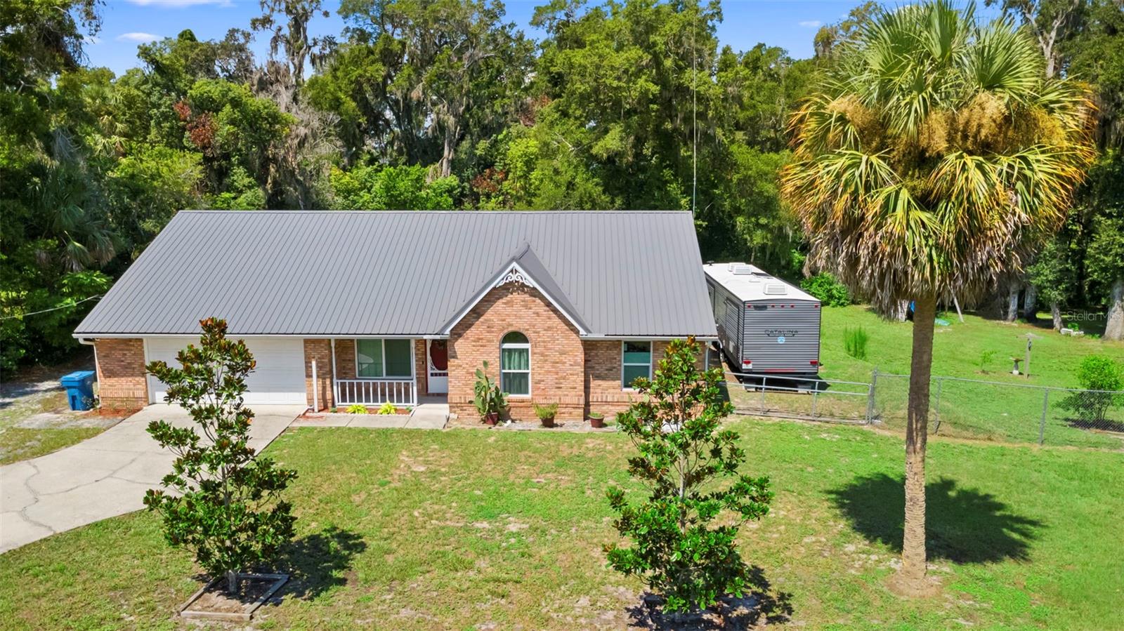 Welcome to this spacious 3 /2 home w/1,888 sq. ft. of comfortable living space on a large .67-acre fenced yard made up by 4 lots. Thoughtful upgrades give this home an important step forward in being ready for a few of your own personal touches & energy. Peace of mind comes w/newer tinted, noise reduction & exterior dust resistant windows (2022), new windows were also outfitted w/custom cordless, light filtering top down/ bottom up honeycomb blinds, along w/newer gutters & beautiful metal roof, colored to complement the traditional red brick exterior (2019). When you enter the home you will notice the beautiful wallpaper that adds charm to the Dining room. Off the entry is the formal dining or bonus room. The solid oak flooring runs throughout the dining & living rooms. The large living room boasts high ceilings, ceiling fan & easy access to the kitchen. The beautifully refreshed (2023) open tiled kitchen featuring new countertops, black stainless defines the newer stove, dishwasher, farmsink w/high faucet. The recently refinished cabinets pop w/color & this space will be your favorite place to be with family. Kitchen also has a butcher block drop island for food prep or enjoying a little meal & a spacious 6’ shelved pantry closet. The Primary Bedroom is spacious & includes a walk-in closet, ceiling fan, skylight & private En Suite bathroom that has a walk-in/handicapped accessible shower. Split plan hosts 2 additional bedrooms w/spacious closets & share a guest bathroom. The Great Room sets behind the living room w/rich cherry colored wood-like planked flooring throughout (2022). A full-bank of custom built-in shelving & study desk add organized storage to this room. At the far end of this great room is a plumbed kitchen sink & cabinet area, which was part of a kitchenette. A semitransparent, modern barn door slides open to reveal a smaller private room which was used as an extra guest bedroom & an additional ¾ bathroom. This area also has its own ceiling fan & light remote combo. The Great Room is filled w/potential, maybe an In-law Suite, guest area or simply creating the perfect gathering space for a growing family. The great room also boasts French doors leading to the covered, screened back porch w/a view of the rambling wood lined, fully fenced backyard. Which also creates a private entrance for the back of the house. The backyard has a custom built playground complete w/swing, slide & 2 climbing walls to an upper play deck, designed to hug one of the many mature, healthy wateroaks. 2 outbuildings, both w/solid entrance decks. The larger, newer one is fully skirted w/a raised ceiling & overhead door. A 6’chain linked fence fully encloses the large backyard & has 3 double sized swing gates. Did we mention the amazing owls? RV Pad is within the fenced back yard along RHF side of home. Pad area is grass, had been bermed up level w/the house. Connections to water, direct sewer line & electricity are there (separate breaker). Garage & back Porch entrances are handicapped accessible. Added security w/flood lights front & back & new ring doorbell. Located within 2 miles of historical downtown, close to schools, shopping, & restaurants, this home combines comfort, flexibility & outdoor space — perfect for a variety of lifestyles. Home is also only 1.5 miles to the Deland Amtrak & Newest Sun Rail Station Stop. Have a boat? This property has plenty of storage area. Home is only 3.8 miles from the popular St. Johns River Marina & Resort