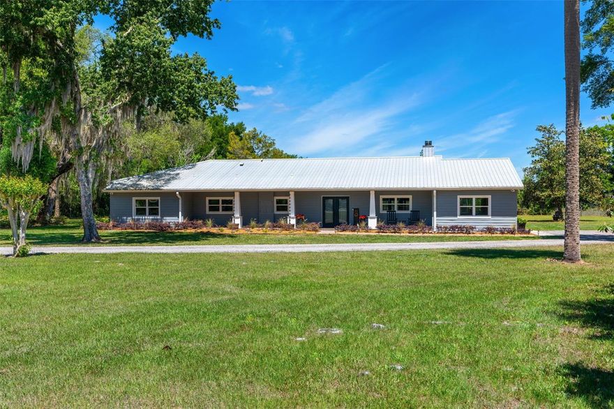 Fully remodeled ranch-style estate offering refined country luxury on just over 10 acres with lake frontage, combining open pasture with natural lakefront terrain. With an effective year of 1990 and significant updates completed between 2021–2023, including major systems in 2021 and interior finishes in 2023, the home blends established structure with modern functionality and design. This 4-bedroom plus den residence features an open floor plan with soaring cathedral ceilings, a wood-burning fireplace with a stone façade, and French doors that open to a screened lanai with tongue-and-groove wood ceilings overlooking the pool and heated spa. The kitchen is both elevated and highly functional with leathered granite countertops, white cabinetry with abundant storage, 2021 appliances, and a walk-in pantry concealed behind custom barn doors, with a laundry room conveniently located just off the kitchen. A matching custom barn door entry leads to the private study/den. The primary suite is privately positioned with direct access to the lanai and includes a large walk-in closet and a well-appointed ensuite with an oversized shower and separate water closet, offering a comfortable and secluded retreat. Two secondary bedrooms feature ensuite bathrooms, while an additional bedroom—currently used as an office—opens to a private side porch through sliding glass doors. Outdoors, the property supports a range of uses including equestrian, hobby farm, or private retreat living, with a lakeside fire pit, open pasture, and a barn with two horse stalls and a tack room with updated electrical (2026). The 3-car carport features an enclosed workspace along with additional open storage, with exterior wood recently replaced (2026). Recent updates include metal roof, HVAC, ductwork, electrical panel, replumb, new drainfield and appliances (2021), along with flooring and cabinetry (2023). An exceptional opportunity for those seeking space, privacy, and a property that is ready to enjoy from day one, with flexibility to live, work, and expand without compromise.