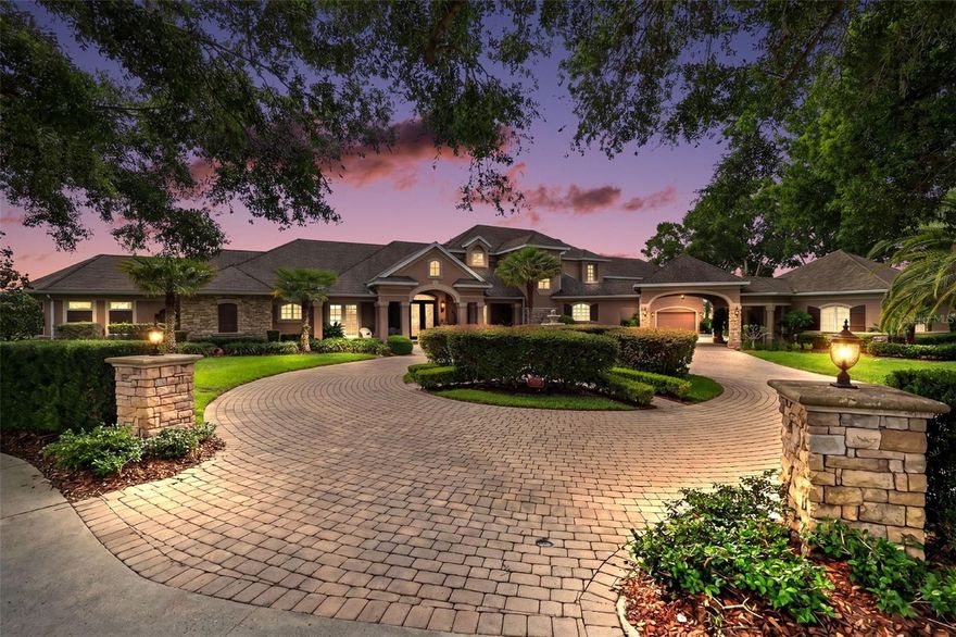 Located in the exclusive gated community of Loch Leven in Mount Dora, this extraordinary custom lakefront estate offers luxury living with breathtaking panoramic views of spring-fed Lake Loch Leven. Situated on 4.55 acres with approximately 200 feet of waterfront frontage, this impressive residence features over 5,600 square feet of thoughtfully designed living space with 5 bedrooms, 4.5 bathrooms, multiple flex spaces, and resort-style outdoor amenities.
From the moment you arrive, the circular paver driveway, porte cochere, stone accents and 2-two car garages create a grand first impression. Elegant leaded glass front doors welcome you into a stunning interior showcasing soaring ceilings, travertine and oak flooring, archways, crown molding, and expansive lake views throughout. The inviting family room features a gas fireplace, dramatic coffered wood ceilings, and spectacular lake views, creating a warm yet elegant gathering space. The spacious chef’s kitchen appointed with granite countertops, stainless steel appliances, gas cooktop, breakfast bar, solid wood cabinetry, and an open layout ideal for entertaining. Multiple living, dining spaces and wet bar flow seamlessly to the outdoor living areas, where an edge-less heated pool & spa, screened lanai, outdoor kitchenette and oversized boat dock with boat slip create the ultimate waterfront retreat.
The thoughtfully designed main floor includes a half bathroom, laundry room, private den/office/library, guest bedroom, full bathroom and office space with direct pool and lanai access, perfectly situated for in-law or guest quarters. The spacious primary suite offers a bonus sitting room, French doors leading to the pool and lanai, walk-in closet, and luxurious ensuite bathroom complete with dual vanities, water closet, walk-in shower, and whirlpool tub.
Upstairs offers 3 additional bedrooms, 2 full bathrooms, storage room and a private movie theater with balcony seating, projector, dumb waiter, ice maker and bar refrigerator. 
Other features include 4 HVAC systems, 2 hot water heaters, new roof 2014, boathouse roof 2020, Simply safe security system, EV charger, Safe room, and abundant storage throughout. The 2-two car garages, covered area, and extended parking offers plenty of room for your toys, family and guests.  Enjoy boating, skiing, and sunset views from your backyard while also taking advantage of Loch Leven’s community amenities including gated entry, tennis courts, playground, and private boat launch. Conveniently located just minutes from historic downtown Mount Dora’s restaurants, shops, and festivals, this exceptional property offers the perfect blend of elegance, privacy, and Florida lakefront living. Some furnishings are negotiable.