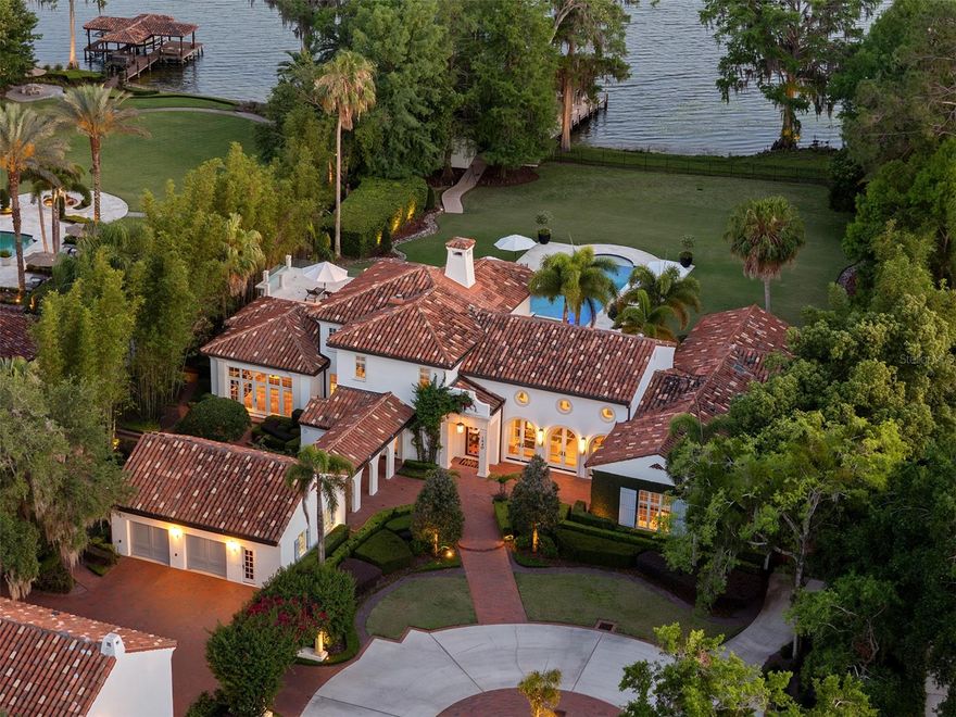 Behind private gates along the shores of Lake Maitland, this elegant Mizner-style Mediterranean estate offers an extraordinary opportunity to own a timeless lakefront masterpiece on the Winter Park Chain of Lakes. Encompassing approximately two acres of meticulously manicured grounds framed by soaring palms and mature live oaks, this exceptional property blends classic architecture with state-of-the-art amenities and modern luxury. Originally built with uncompromising craftsmanship and fully renovated in recent years, the home’s interiors, designed by Ted Maines, exude sophistication, featuring curated high-end finishes, custom built-ins, and designer lighting throughout. The main house offers 6,634 square feet while the detached media room has 676 square feet, and the second-floor guest apartment above the media room has 864 square feet. The main residence includes four spacious bedrooms, each with en-suite baths and walk-in closets, as well as a stately office/library and a stunning grand Mizner trademark living room with a soaring 24-foot wood-beamed ceiling. This additional entertaining area is flanked by two walls of arched French doors, one offering breathtaking views of Lake Maitland and the other opening to a tranquil courtyard, creating a seamless connection to the home’s beautifully designed outdoor spaces. A dramatic formal dining room showcases a curved wall of windows that frame spectacular lake vistas, while the chef’s kitchen is equipped with commercial-grade appliances and opens to a gracious gathering room ideal for everyday living and casual entertaining. Upstairs, the luxurious primary suite serves as a private retreat with its fireplace, a spacious custom dressing room, a spa bath with soaking tub and steam shower, and access to a rooftop terrace with glass railings and panoramic lake views. A separate structure on the property includes a state-of-the-art theater/listening room and a fully appointed one-bedroom guest apartment above, complete with a kitchen and living area. Outdoor living is equally impressive, with a covered lanai and summer kitchen off the family room, an expansive open-air terrace extending from the great room and a resort-style travertine pool deck surrounded by lush landscaping. A newer Trex walking path leads to the covered boat dock with lift, complete with a jet ski lift, conditioned storage room and direct access to the Winter Park Chain of Lakes. Additional features include four EV chargers, a Lutron smart lighting system, a 12-camera security surveillance system with HomeKit integration, high-speed fiber internet from three providers, and a 500-gallon water reserve supporting the fire sprinkler system in the main house. A circular paver driveway, with automated gate entry and a generous motor court completes the approach. In one of Maitland/Winter Park's desirable lakefront enclaves, this private estate offers unmatched serenity and convenience just minutes from Park Avenue’s renowned shops and restaurants, area hospitals, major roadways, and both the executive and international airports. See MLS attachments for a list of additional enhancements to the property by owner.