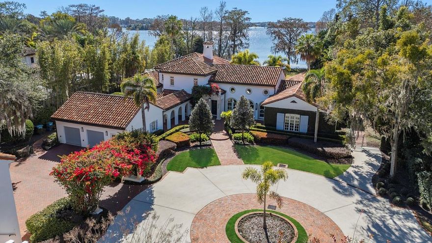 Villa Serenata, a lakefront legacy on Lake Maitland. Behind private iron gates along the storied shores of Lake Maitland, Villa Serenata presents a rare opportunity to own a distinguished Mediterranean estate on the renowned Winter Park Chain of Lakes. On approximately two acres of meticulously curated grounds, this extraordinary residence feels less like a home and more like a private resort, crafted for those who appreciate timeless architecture, thoughtful design and elevated lakefront living. A sweeping circular driveway welcomes you beneath a canopy of soaring royal palms and majestic live oaks, immediately setting the tone for what lies beyond. As the automated gate opens, the property reveals itself as a serene sanctuary where elegance and privacy coexist in harmony. The 6,634-square-foot main residence showcases interiors by acclaimed designer Ted Maines, unfolding across two levels of refined sophistication. The Mizner-inspired living room commands attention with dramatic 24-foot wood-beamed ceilings and twin walls of arched French doors, one framing sweeping views of Lake Maitland’s shimmering waters, the other opening to a sun-dappled courtyard where mornings naturally begin with coffee and quiet reflection. The upper level is devoted entirely to the primary suite, creating a private retreat complete with a heatless gas fireplace, spa-caliber bath with soaking tub and steam shower, a bespoke dressing room with custom built-ins, and a rooftop terrace with glass railings offering remarkable lake views. Three additional bedroom suites, each with an en-suite bath and generous walk-in closet, provide comfort and privacy for family and guests alike. At the heart of the home, the chef’s kitchen is equipped with Sub-Zero and Wolf appliances, custom cabinetry, and an expansive prep island designed to transition seamlessly from intimate family meals to catered gatherings of 50. The formal dining room features a dramatic curved wall of windows, turning every meal into a lakefront experience, while the richly paneled library and office offer a quiet space for focused work or relaxed reading. Complementing the main residence is a thoughtfully designed guest compound totaling 1,540 square feet. A private media pavilion delivers a state-of-the-art theater and listening room for film enthusiasts and audiophiles, while the one-bedroom guest apartment above provides a fully appointed living space with kitchen, living area and private entry, ideal for extended family, visiting guests or live-in staff. Outdoor living is equally exceptional. Resort-style travertine surrounds the pool amid lush tropical landscaping, creating a tranquil setting for sun-filled afternoons. A covered lanai with full summer kitchen flows effortlessly from the family room, while an expansive open-air terrace extends from the great room, an inviting backdrop for sunset cocktails overlooking the lake. Villa Serenata is more than a residence, it is a legacy estate, offering privacy, architectural distinction, and a lifestyle centered on one of Winter Park’s treasured waterfront settings.
