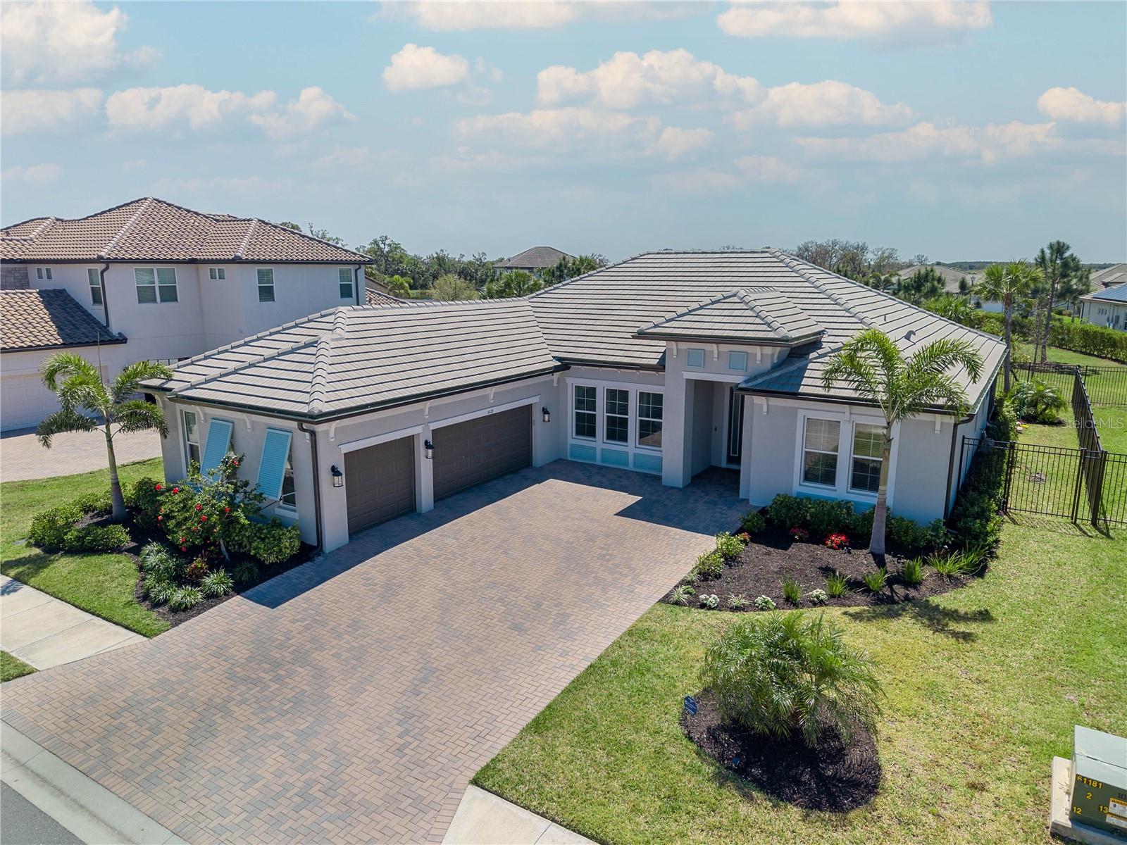 Elegant West Indies-Inspired semi-custom Home in Rivo Lakes – Move-In Ready! Nestled behind the gates of Rivo Lakes, this stunning 2023-built home blends timeless elegance with modern convenience. Its impressive West Indies-inspired facade and lush tropical landscaping create a captivating first impression. Step inside to discover a spacious, open floor plan with soaring ceilings, luxury vinyl flooring throughout, and 8' interior doors for a grand feel. Tray ceilings in the living room and primary suite add an extra touch of sophistication. Smart home features and impact windows provide peace of mind, while the upgraded laundry room cabinetry adds functionality. With 3 spacious bedrooms, 2 luxurious bathrooms, a den, formal dining room, and breakfast area, this home offers ample space for entertaining or everyday comfort. The gourmet kitchen is a chef’s dream, featuring custom cabinetry, matching granite countertops and backsplash, high-end stainless steel appliances, and a cozy café dining nook. A massive granite center island with counter-height seating flows seamlessly into the expansive family room, perfect for gatherings. The primary suite, set in its own private wing, is a true retreat. Enjoy a spa-like en-suite, and an oversized walk-in closet. The lanai provides an ideal spot for your morning coffee and for relaxing with friends and family. The outdoor gas barbecue makes entertaining effortless, and the extended driveway ensures plenty of parking for guests. Why wait for new construction when you can move into this better-than-new custom home today? Whether you're teeing off at a nearby golf course or sipping cocktails with friends, this home is the perfect backdrop for your lifestyle. Don't miss out on this gorgeous home—schedule your showing today!